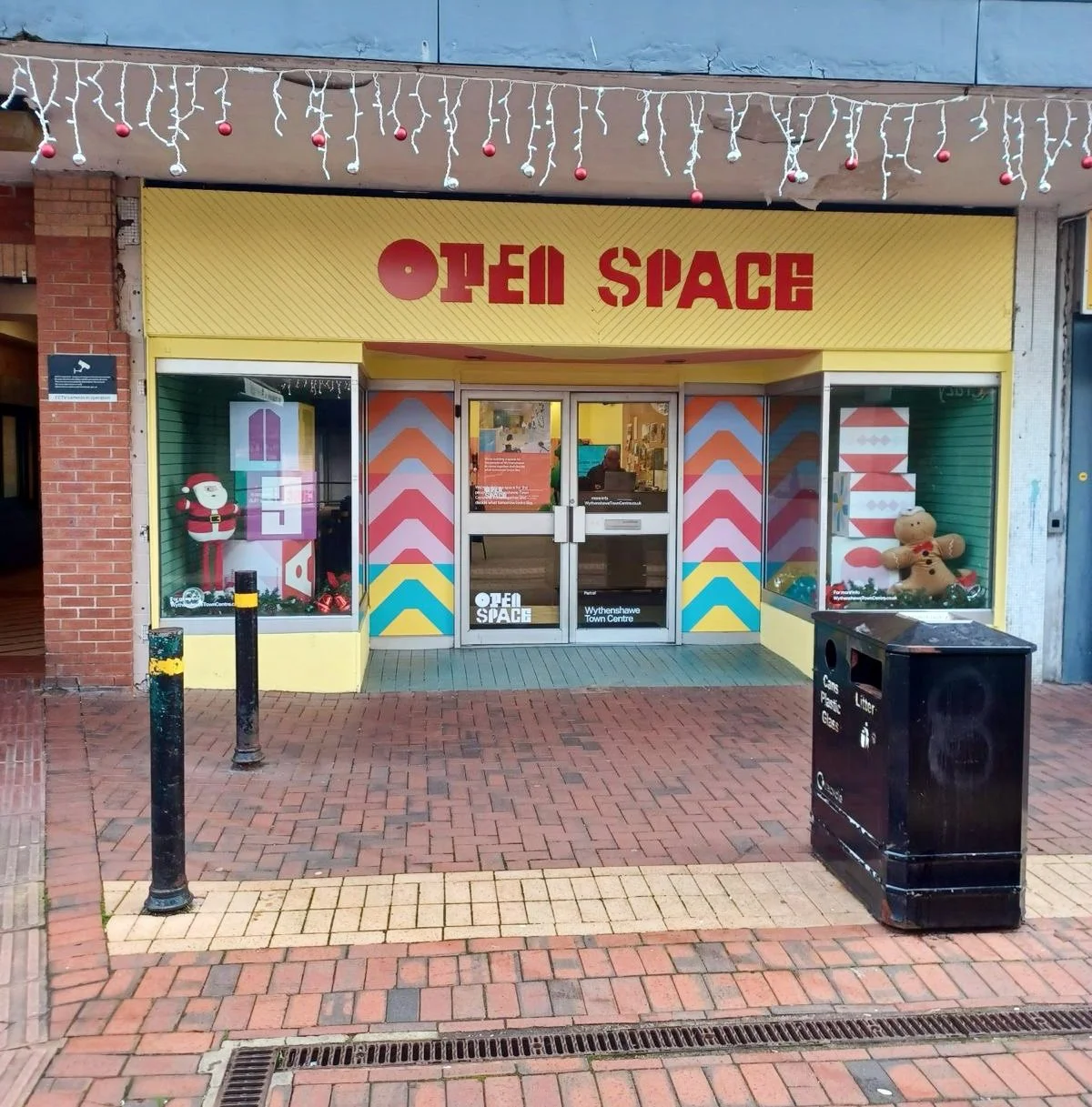storefront with colorful geometric patterns and Christmas decorations, including a Santa and a gingerbread man, on display in two windows, hinting at a Christmas-themed or holiday-related store or event.