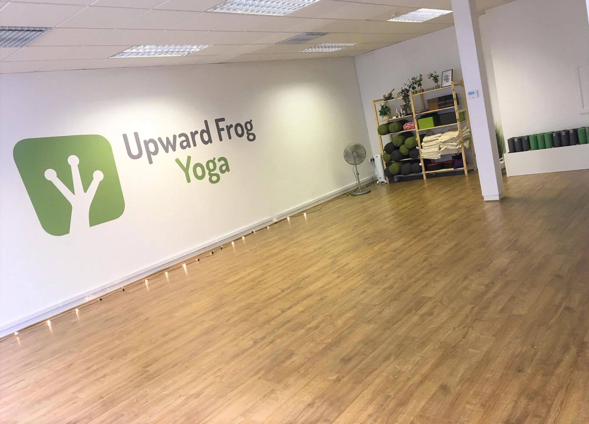 Interior of a yoga studio with a wall that reads 'Upward Frog Yoga' and a logo of a stylized frog.