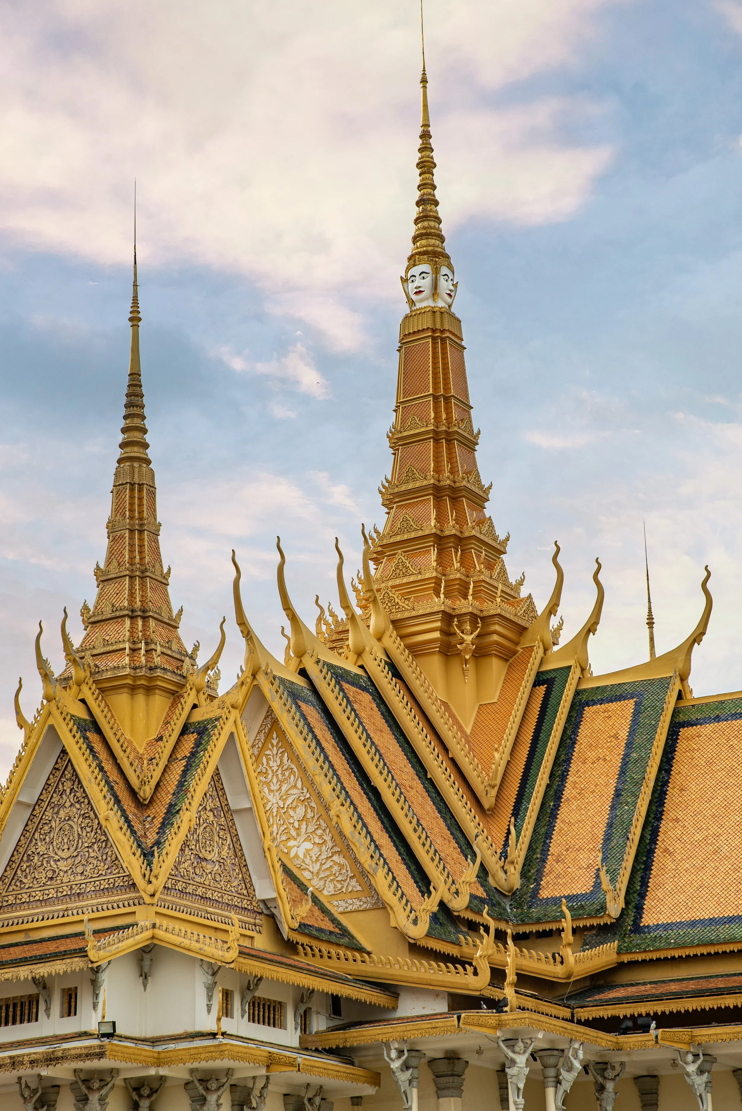 Golden temple roof with intricate details and tall spires against a cloudy sky.