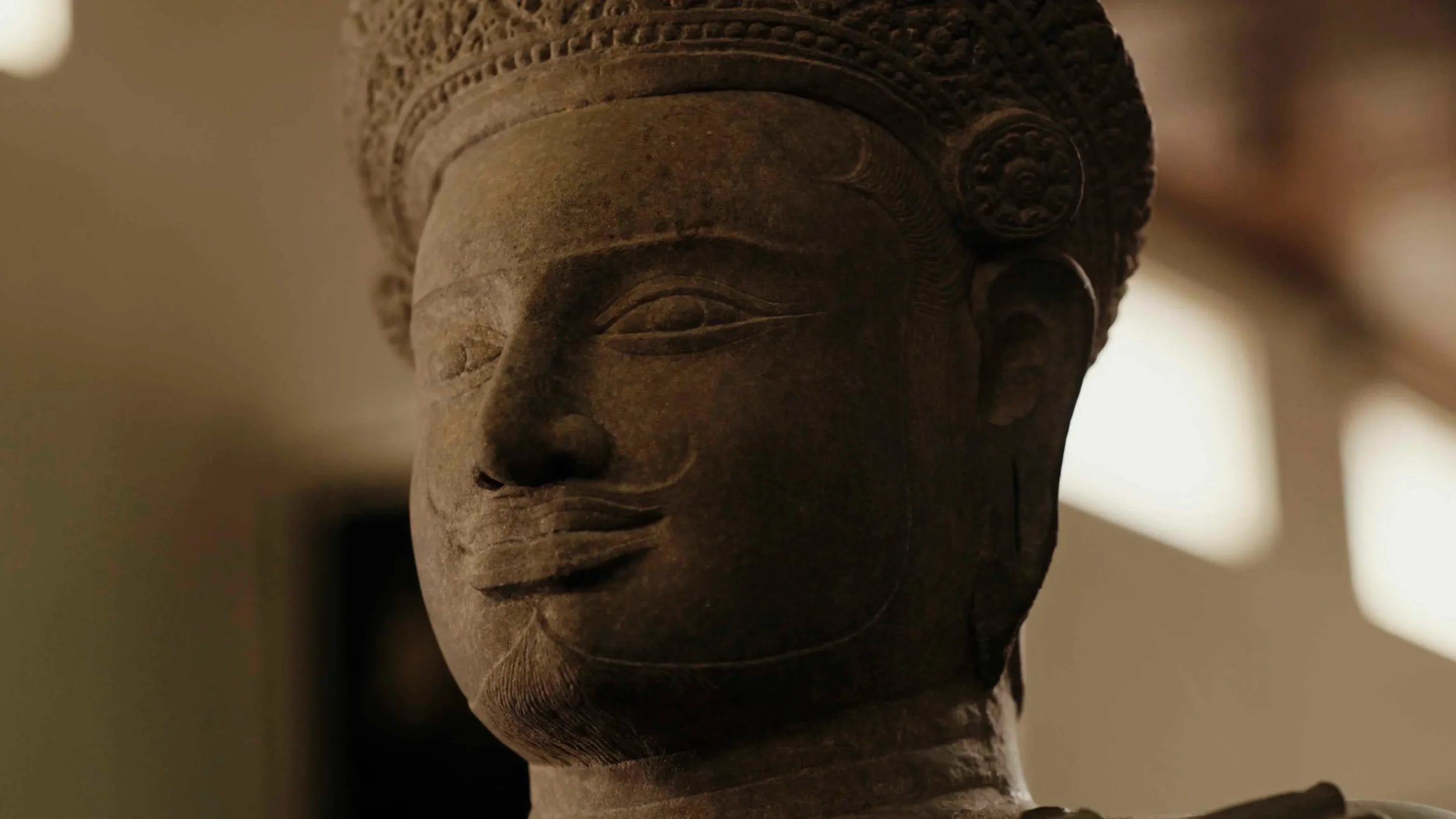 Close-up of an ancient stone sculpture of a human face with detailed facial features and a decorated headdress.
