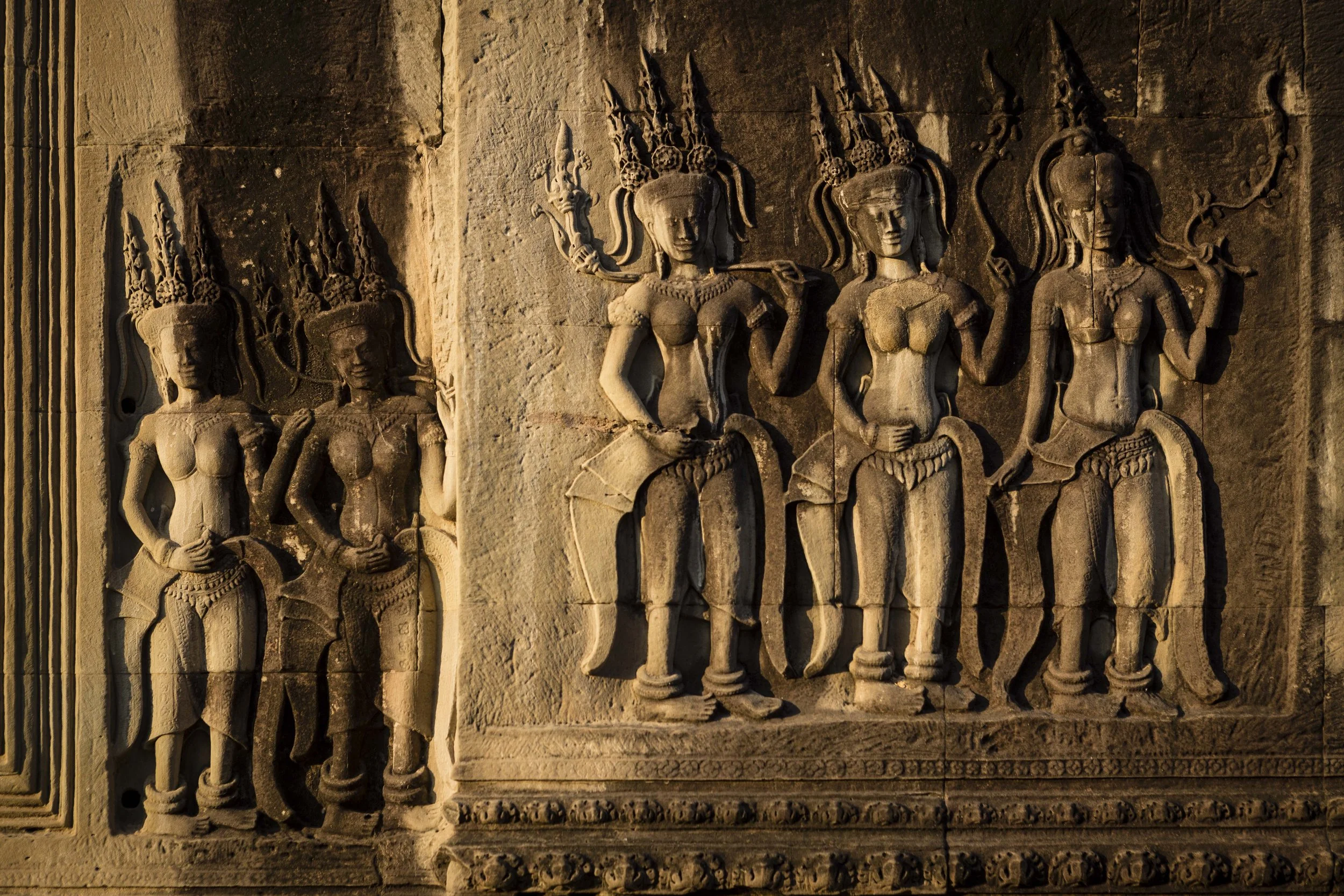 Ancient stone carvings of five standing female deities, each with elaborate headdresses and jewelry, on a temple wall.