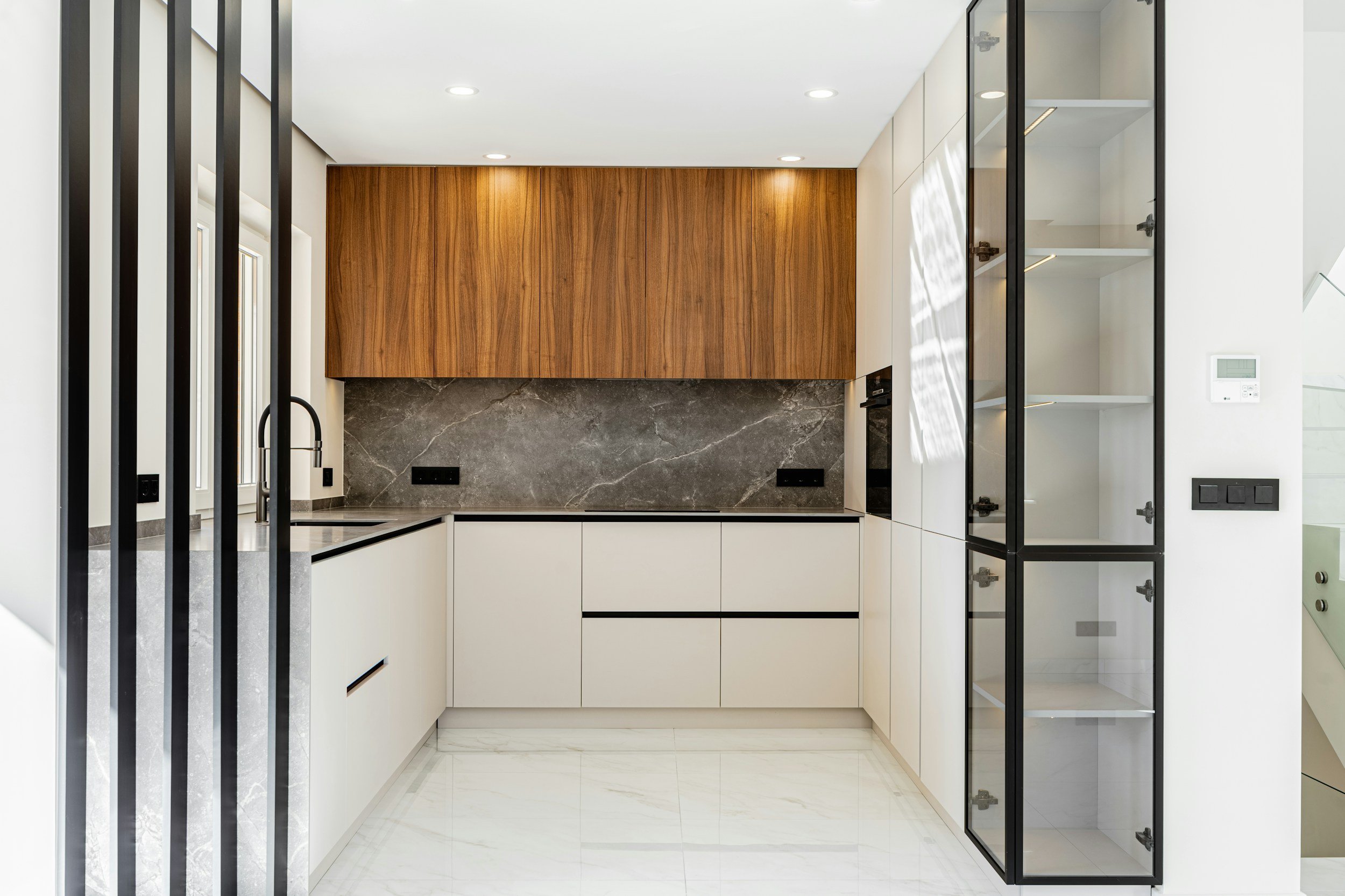 Modernikoe keittiö, valkoiset kaapit, harmaa kivi ja puu sisustuksessa.