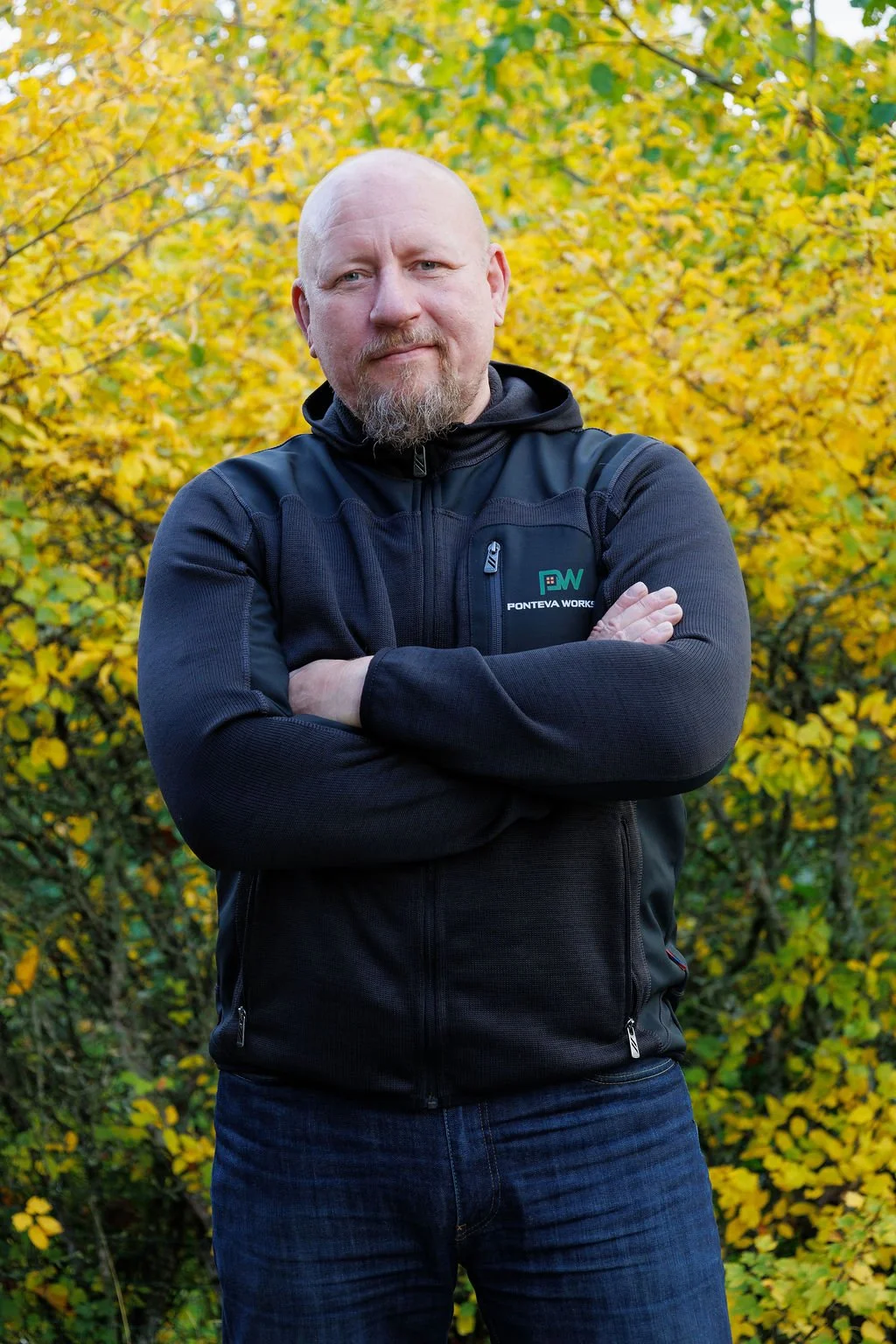 Ponteva Works Henri seisoo kädet ristissä syksyisessä puistossa, taustalla keltaiset lehtikasvit.