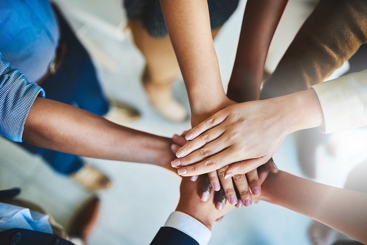 Multiple diverse hands stacked together in a gesture of teamwork.