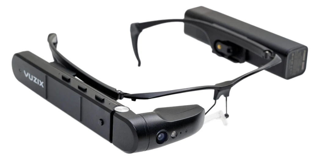 A pair of black smart glasses with a built-in camera and a small display on the right side, labeled 'Vuzix'.