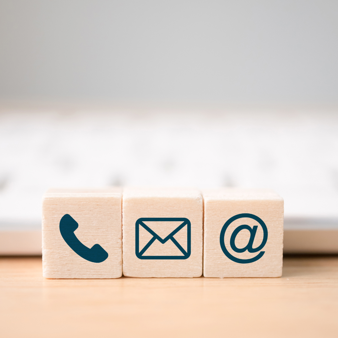 Three light wood blocks with black icons of a phone, envelope, and at symbol, placed on a wooden surface.
