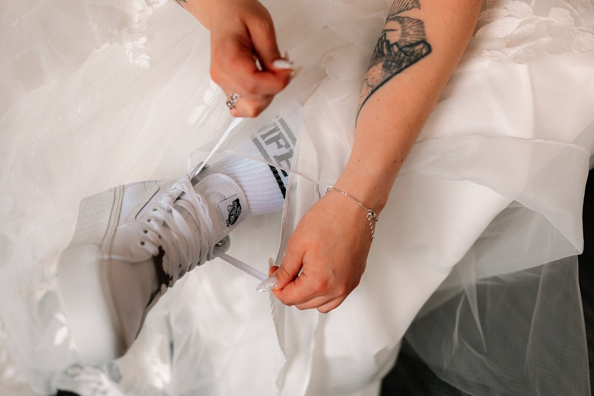  A bride ties the laces of a pair of platformed white Vans trainers wearing white socks that say wifey 