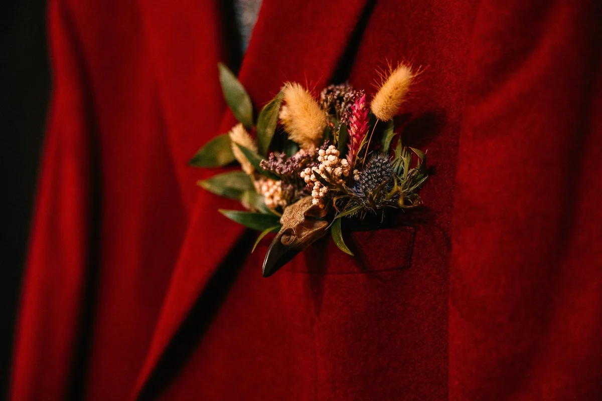  A rustic button hold with a small bird skull attached to a red blazer 