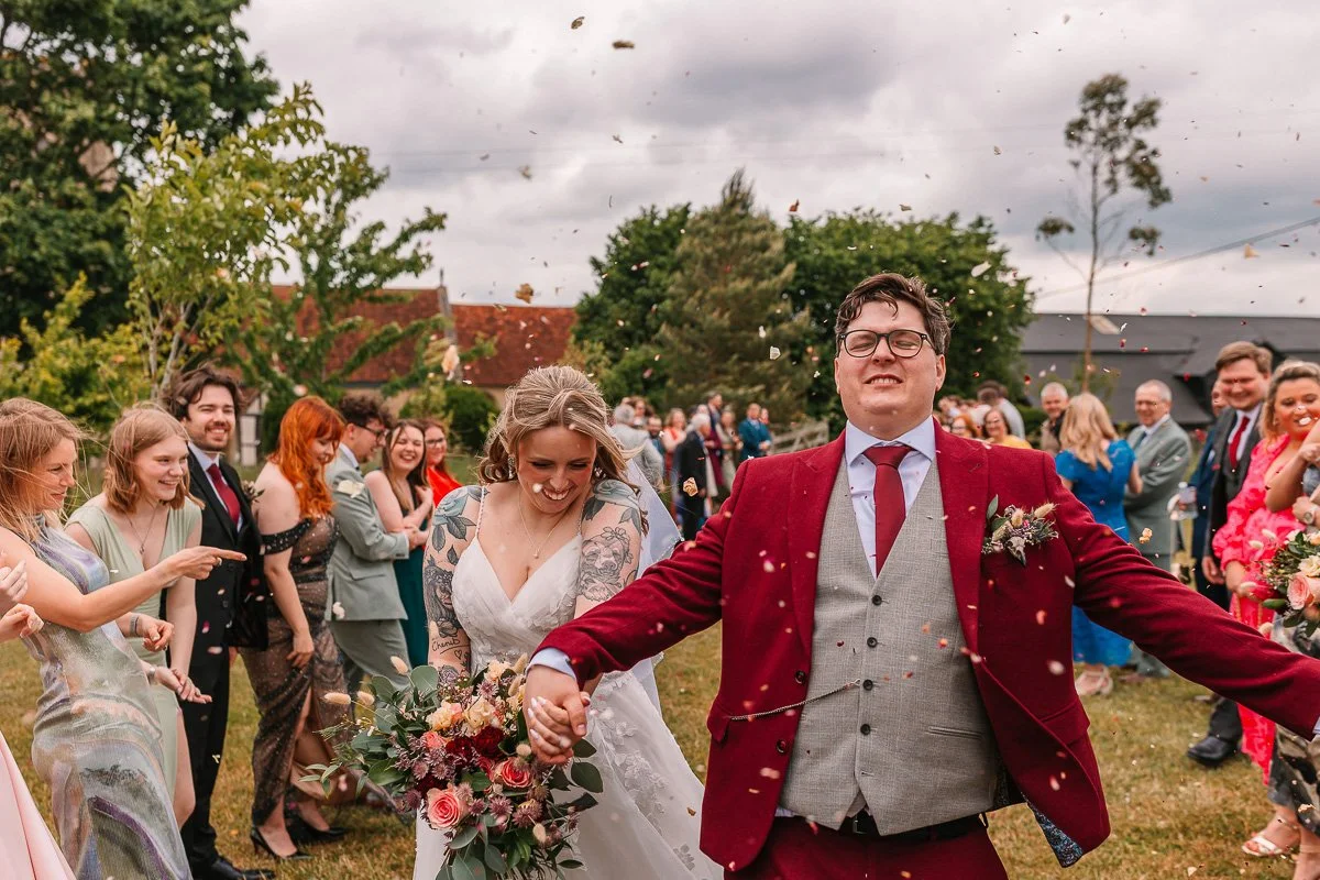  A bride and groom walk though a confetti aisle of real petals being thrown at them 