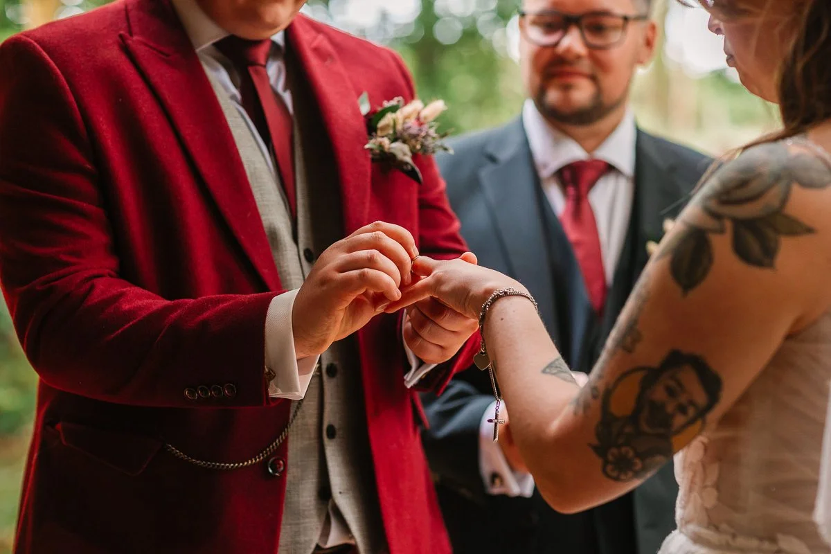  A close up photo of a groom placing a ring on his wife’s hand 