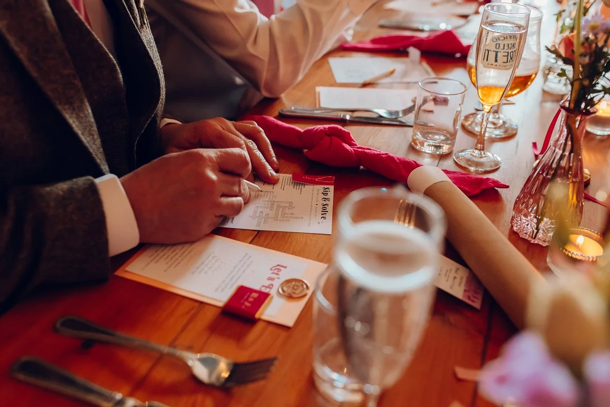  A close up photograph of someone’s hand doing a word search before the wedding dinner.  