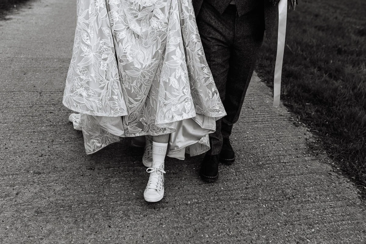  A black and white image of the couples feet as they walk, the bride is wearing converse and bride socks 