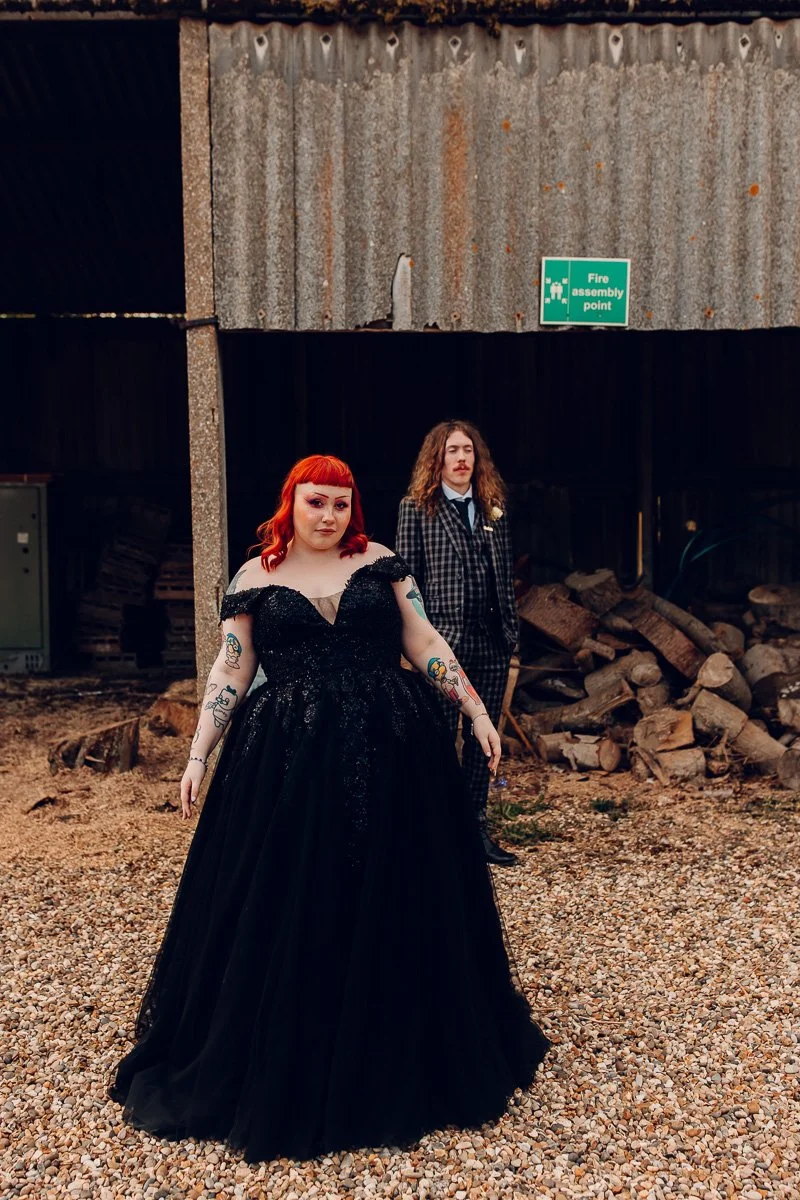 Alternative bride wearing a black wedding dress stands in front of her husband for creative portraits