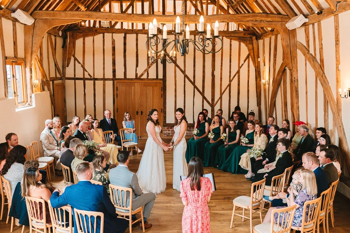 two brides stand in the middle of their ceremony with guests seating in a half moon shape around them
