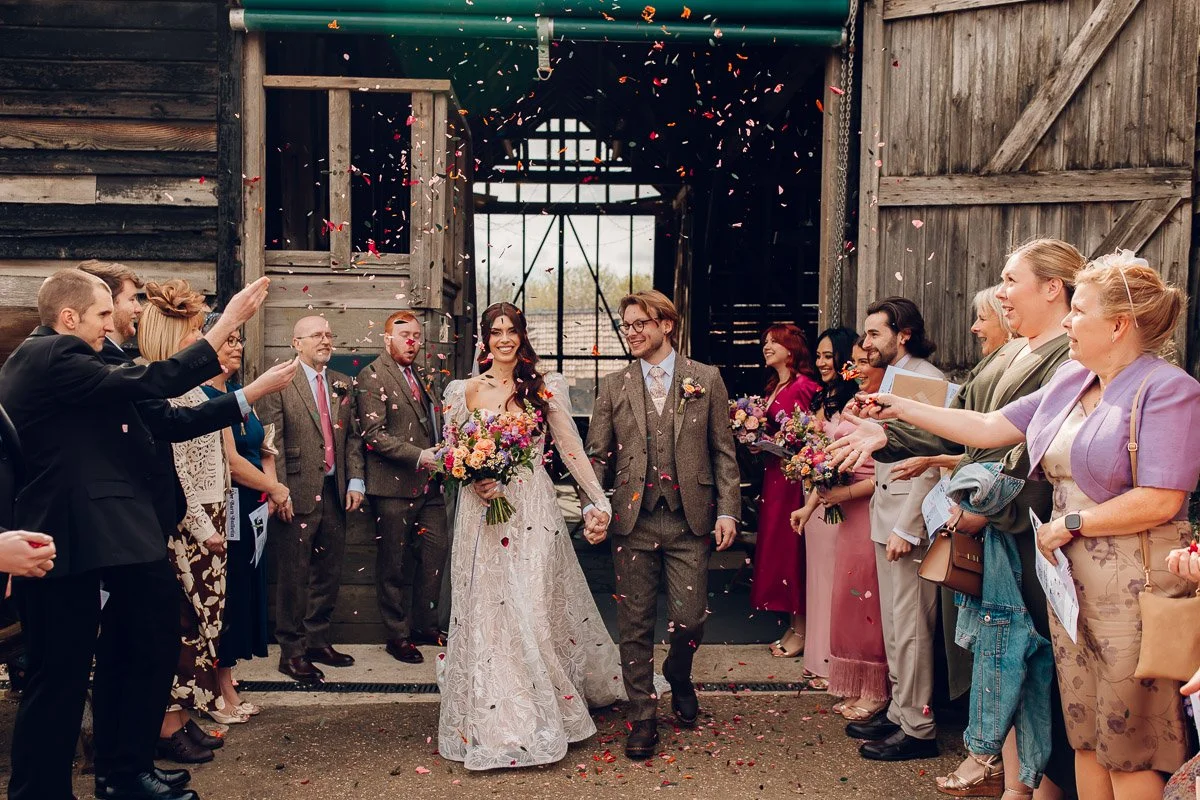 A couple walk hand in hand whilst their guests throw confetti on them at lodge farm barns