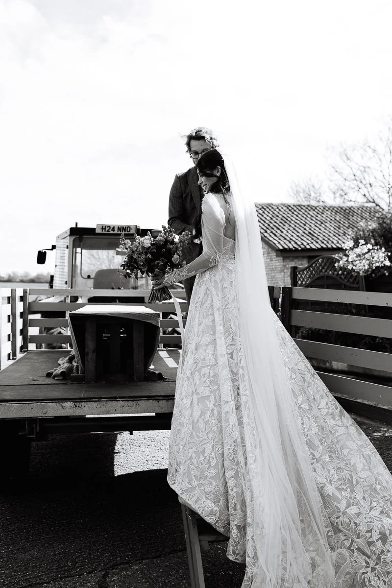 A black and white photo of the bride being helped onto the tractor trailer by her groom