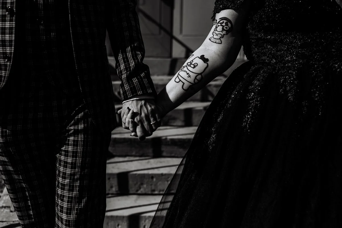 a black and white photograph of a tattooed bride and groom holding hands at houchins wedding venue