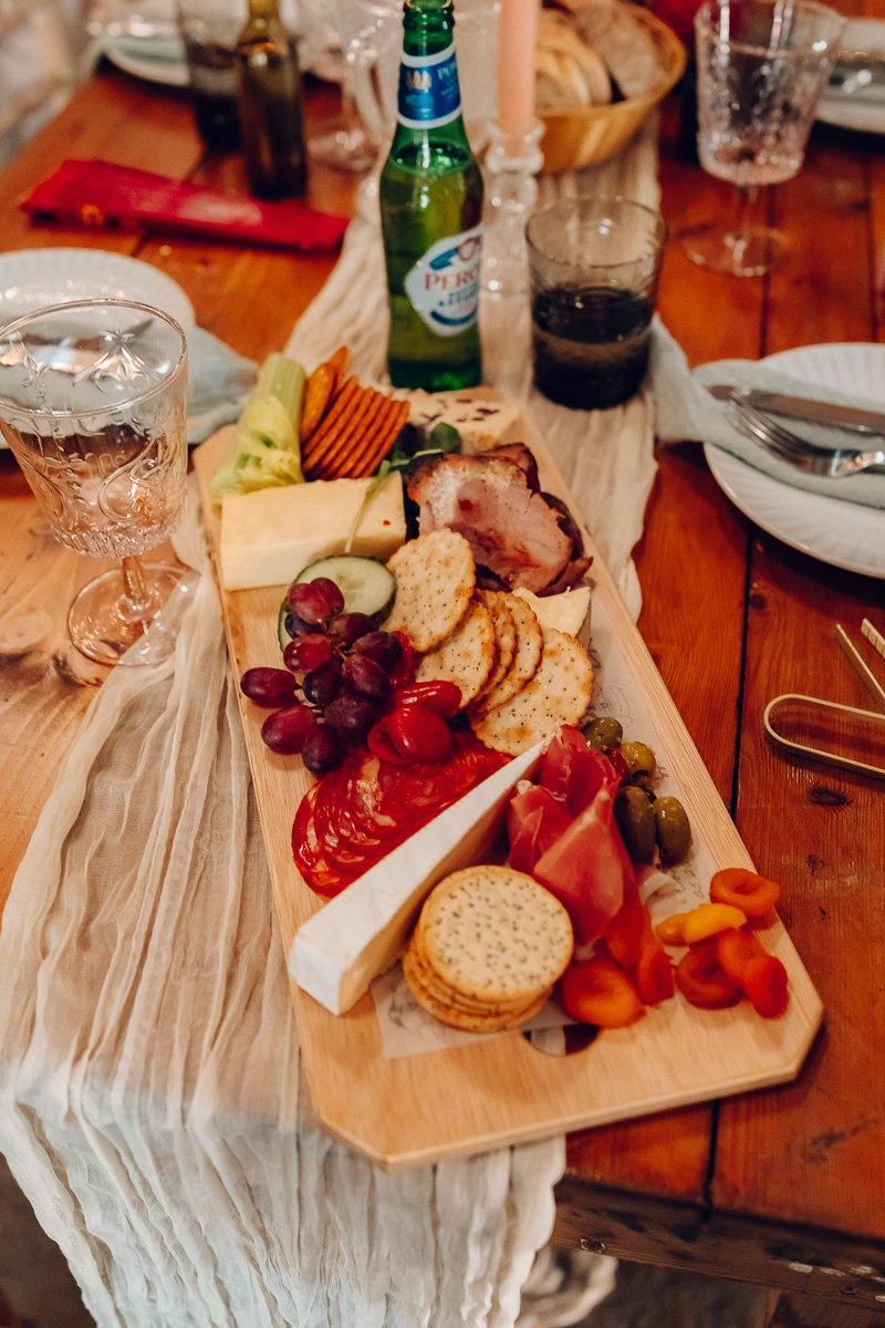 A wooden board full of cheese, crackers and meats is laid out on a wooden table at captain's wood barn