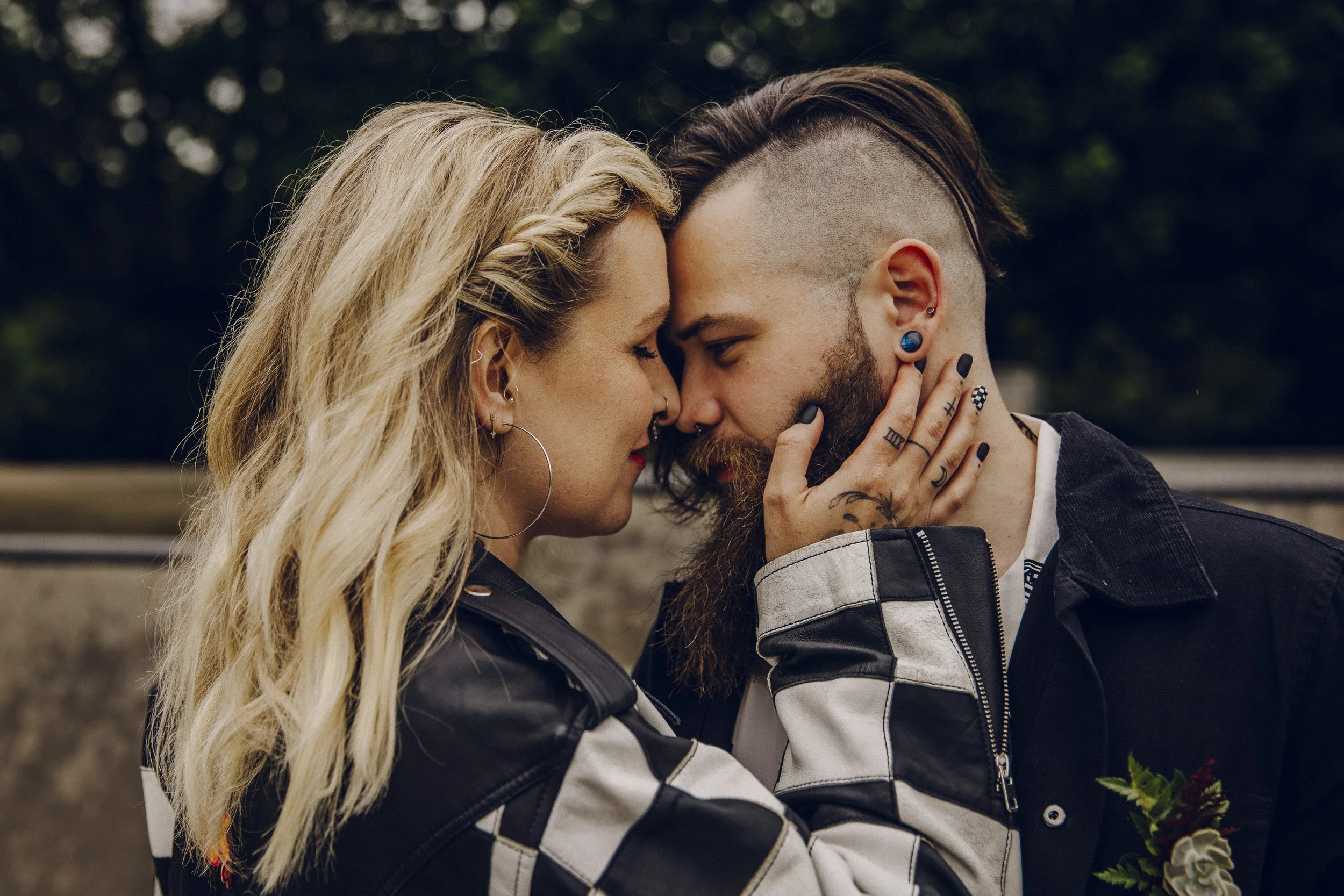 A bride wearing a chequerboard jacket pressers her face to her husbands and holds onto his beard lovingly