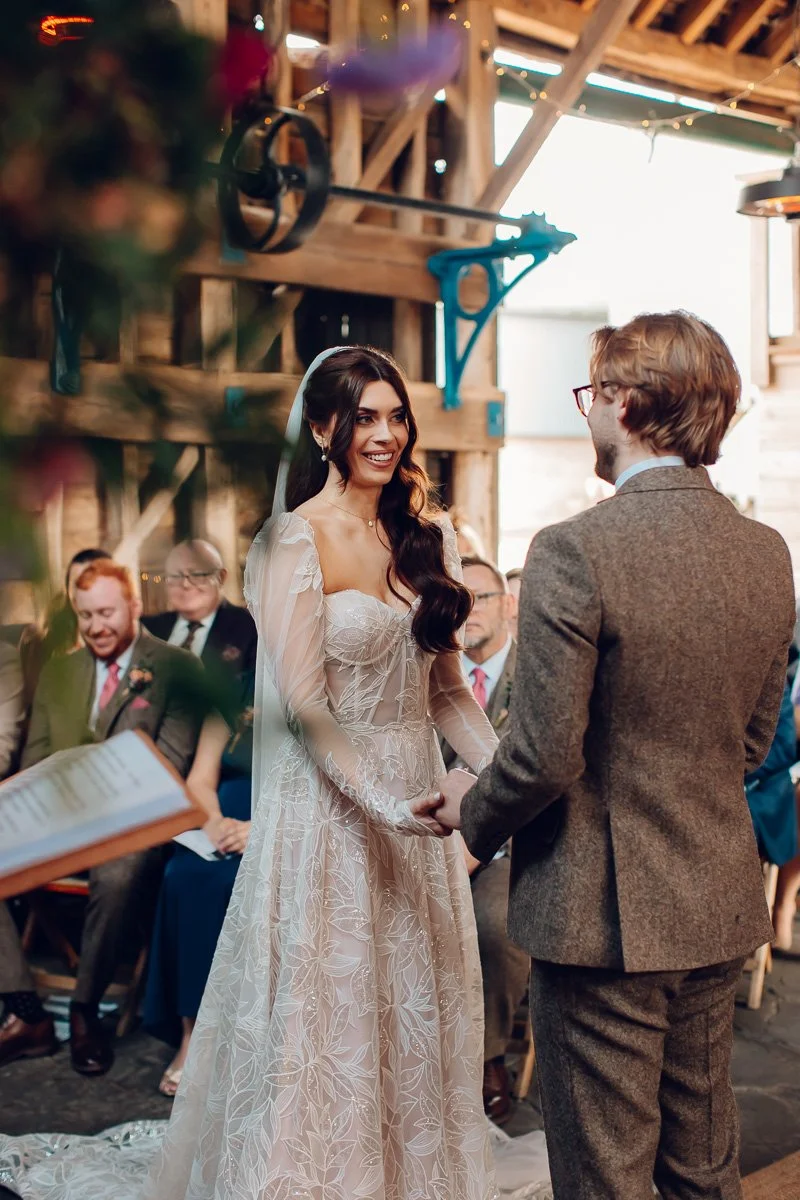 A bride smiles at her groom during their ceremony at the Granary in lodge farm barns