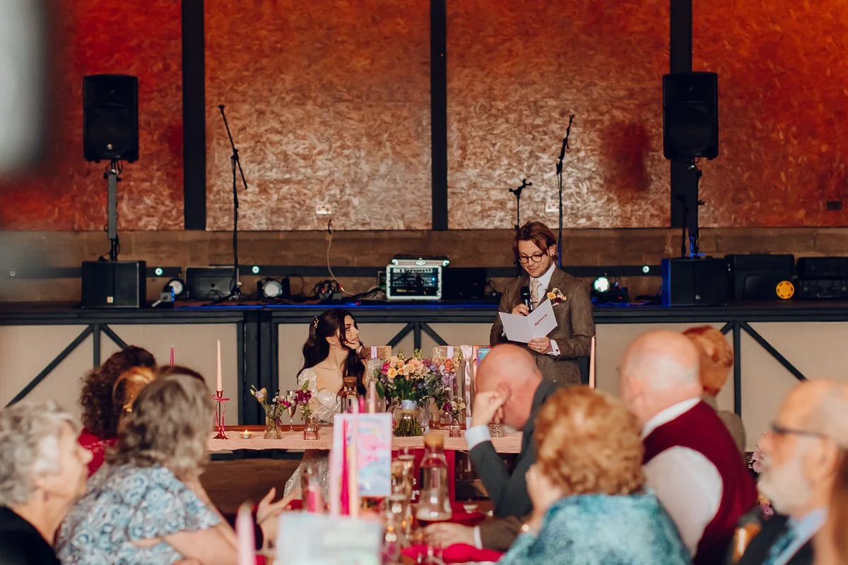 People sit watching on as the groom stands and reads his speech to his bride