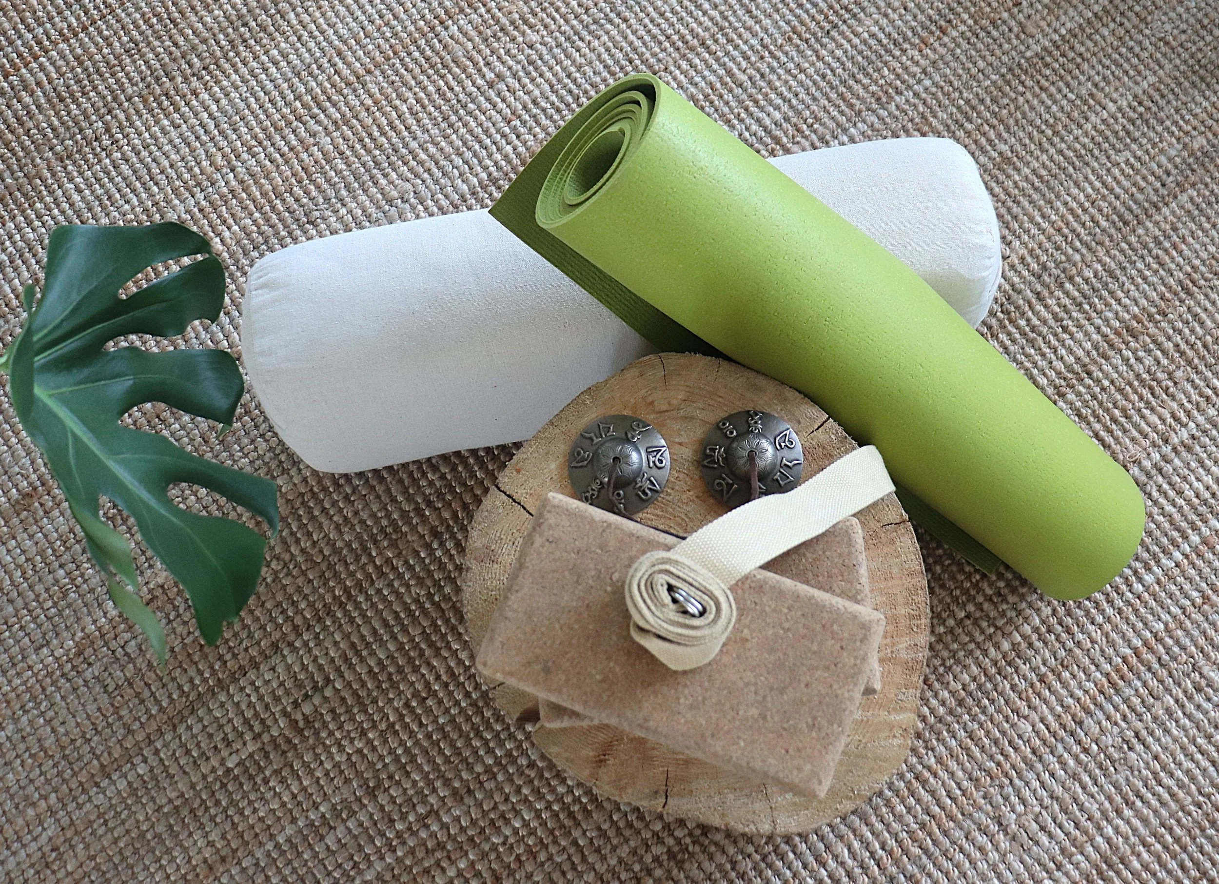 Groene yoga matrol op een witte bank, naast een stuk hout met metalen cijfers, onder een entblad op een tapijtvloer in Amedee praktijk in Rotterdam Zuid