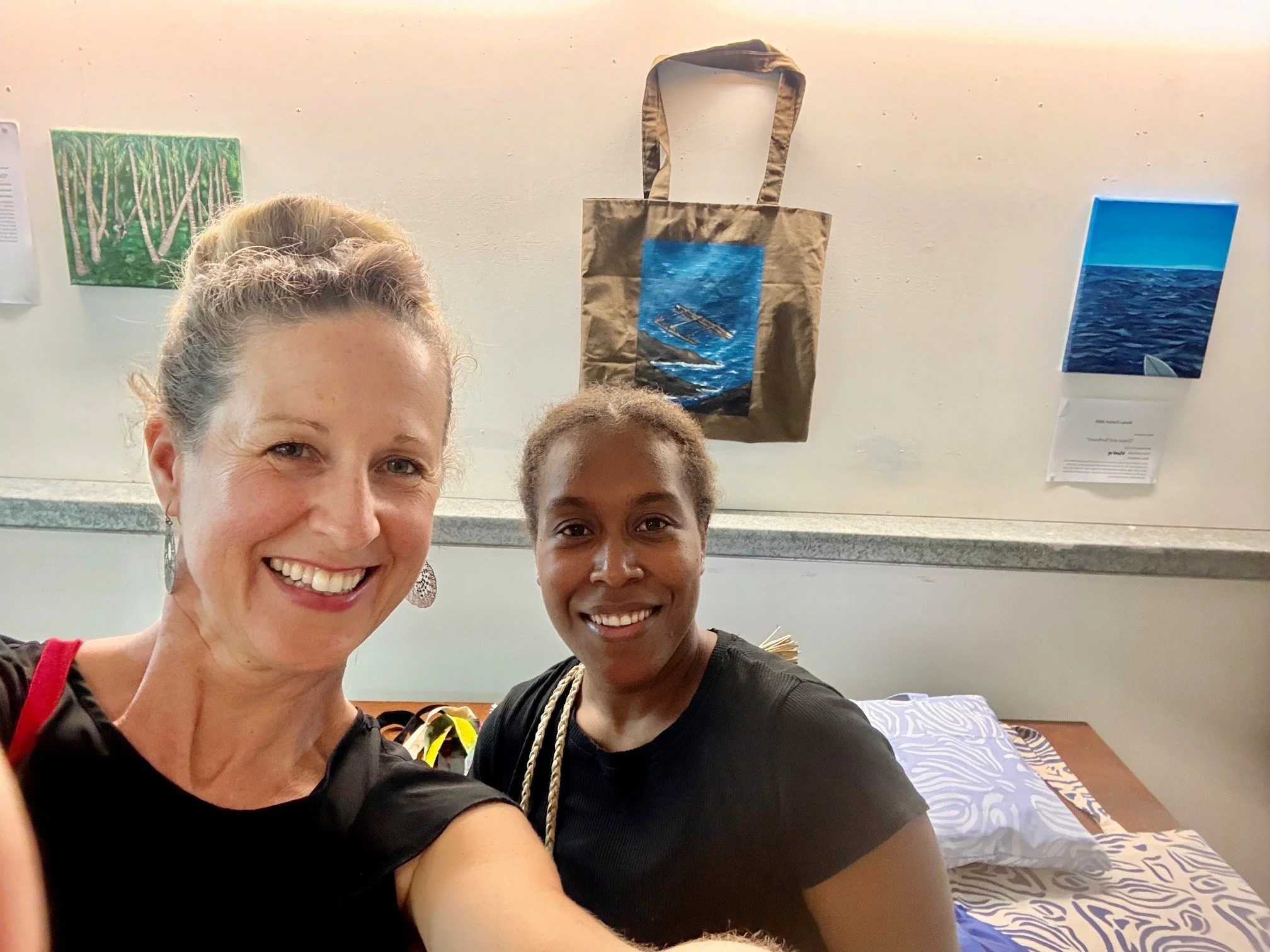 Two smiling women taking a selfie in a room with artwork and a bed in the background.