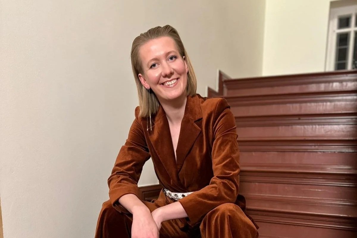 Junge Frau in braunem Anzug sitzt auf einer Treppe und lächelt.