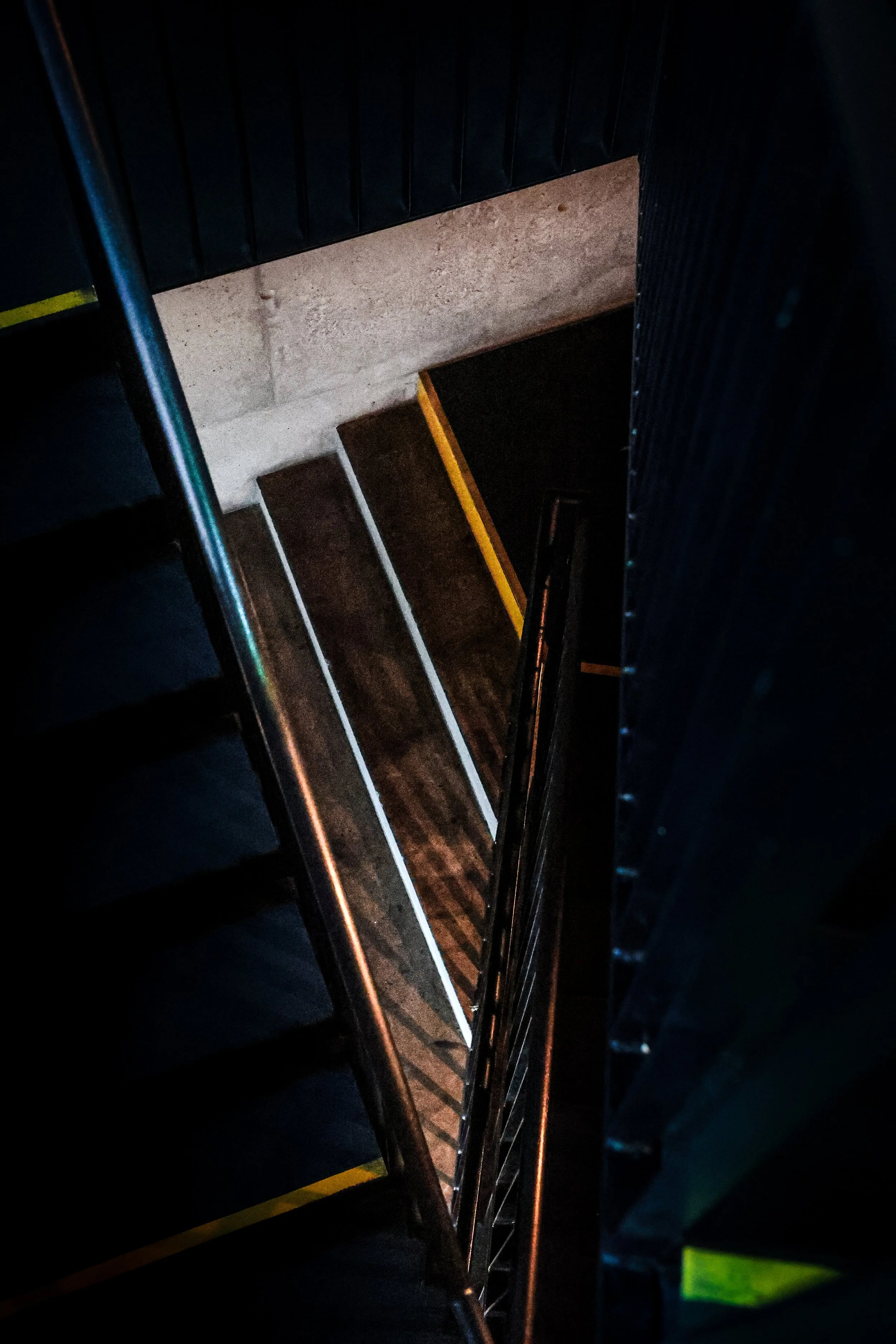 The photo shows a view down a dark staircase with metal railings and dark wood steps, partially illuminated.