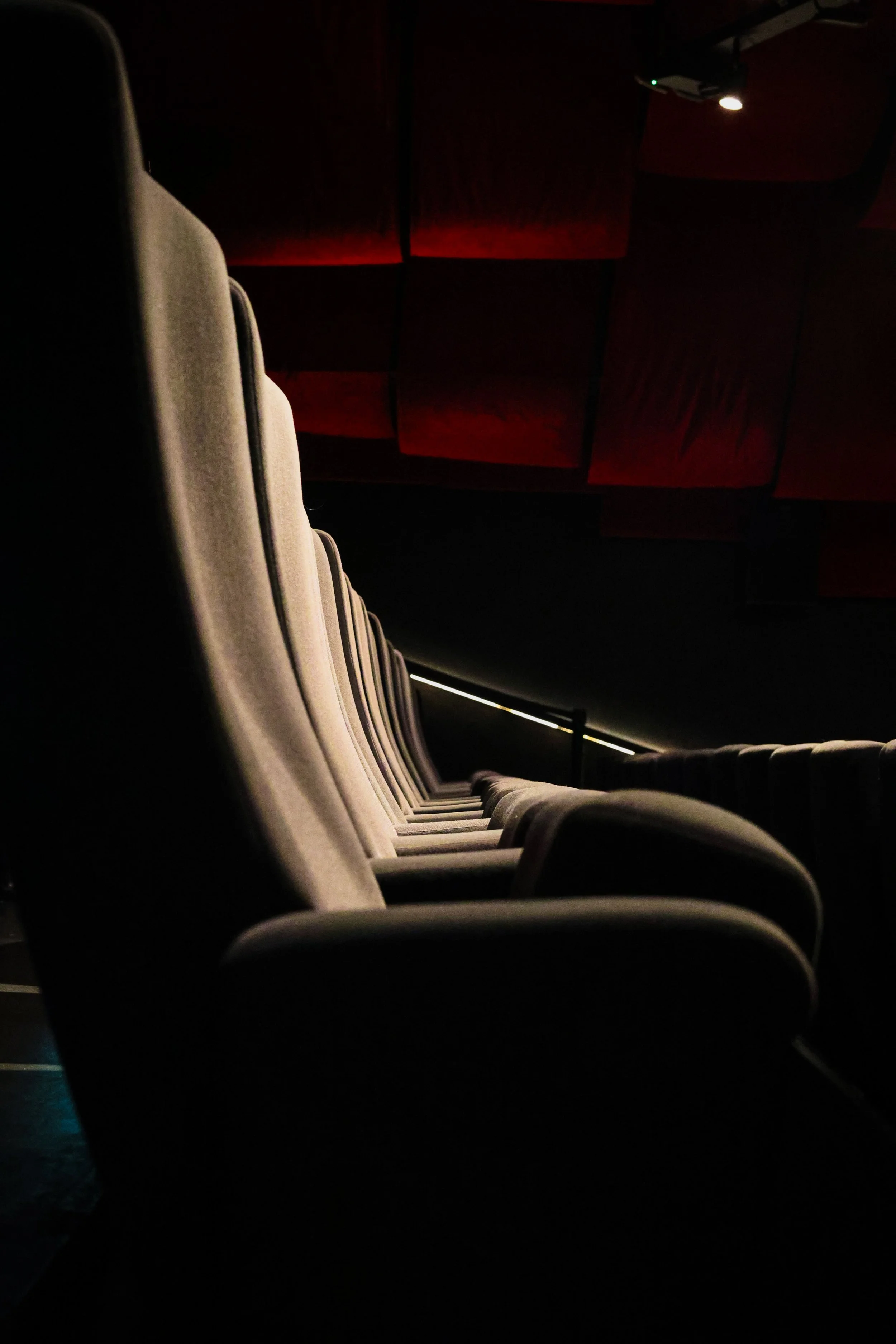 Empty movie theater seats in a dimly lit auditorium with red walls and overhead lighting.