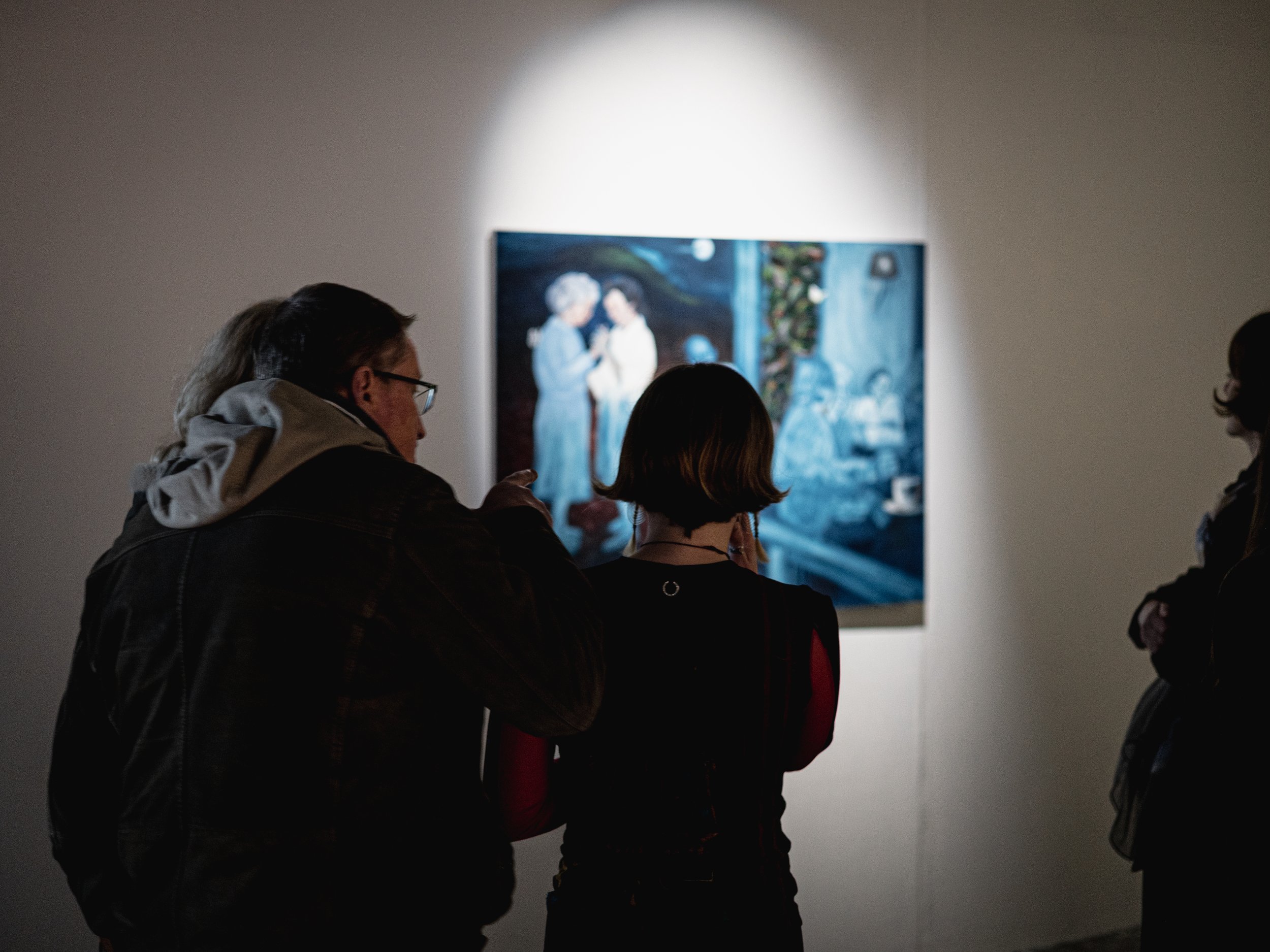 People viewing a painting in a dimly lit art gallery.