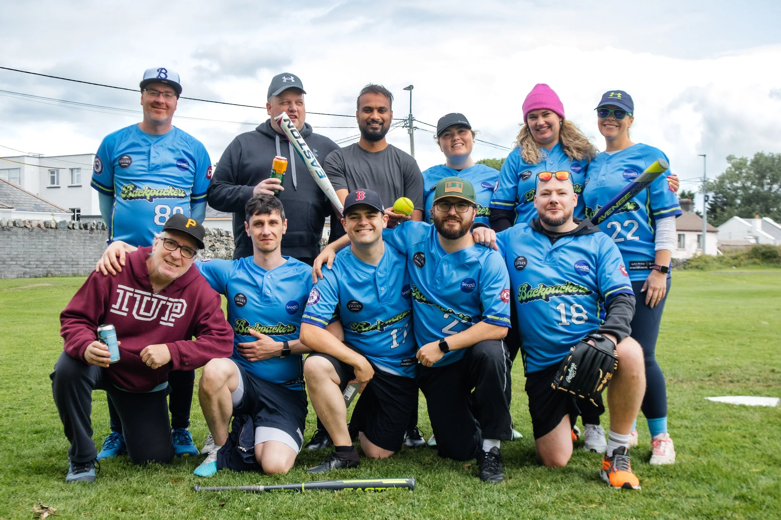 Group of people in baseball uniforms and casual clothing posing on a grassy field
