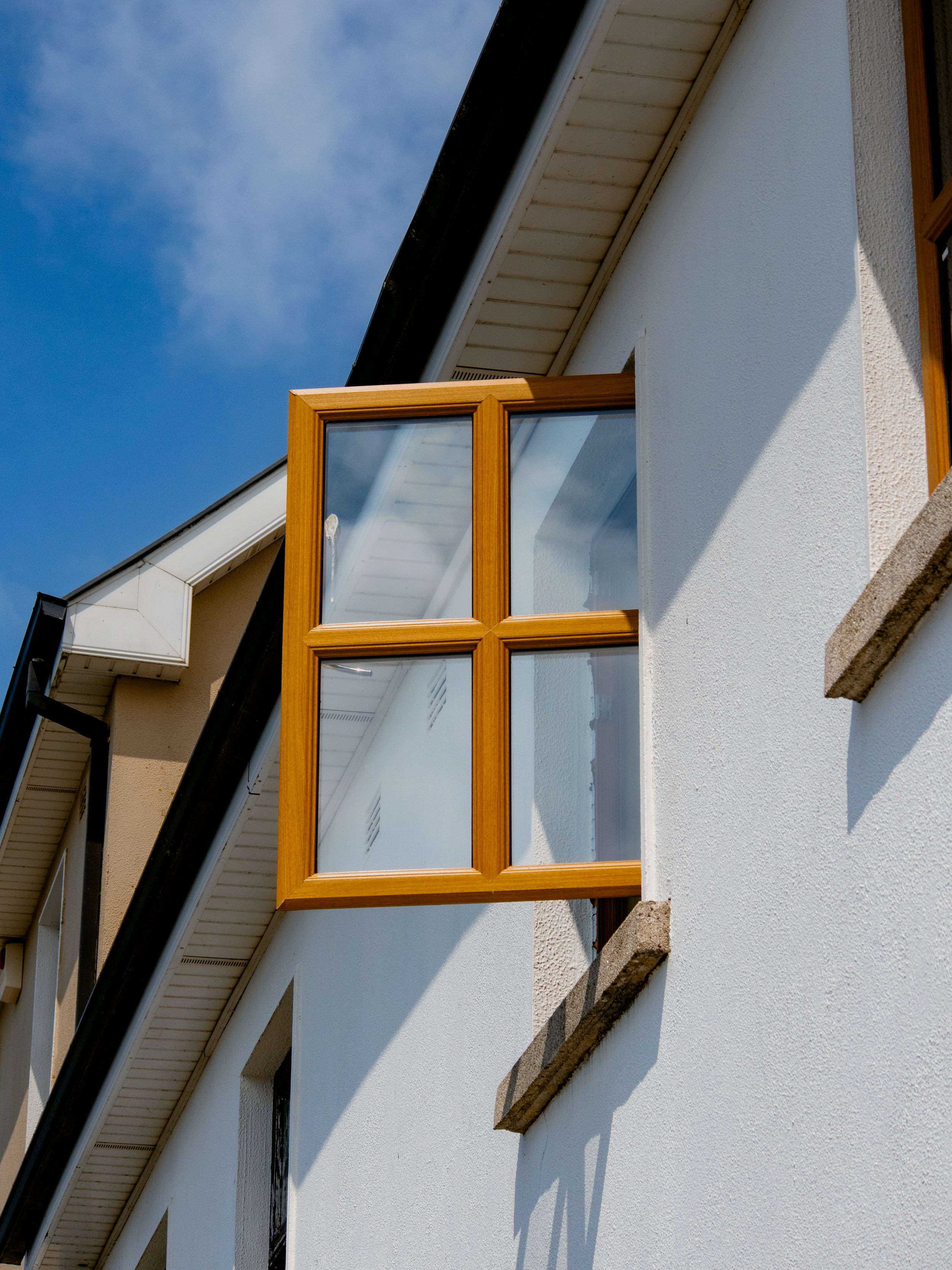 Close-up of an exterior window with wood framing on a white stucco house under a blue sky.