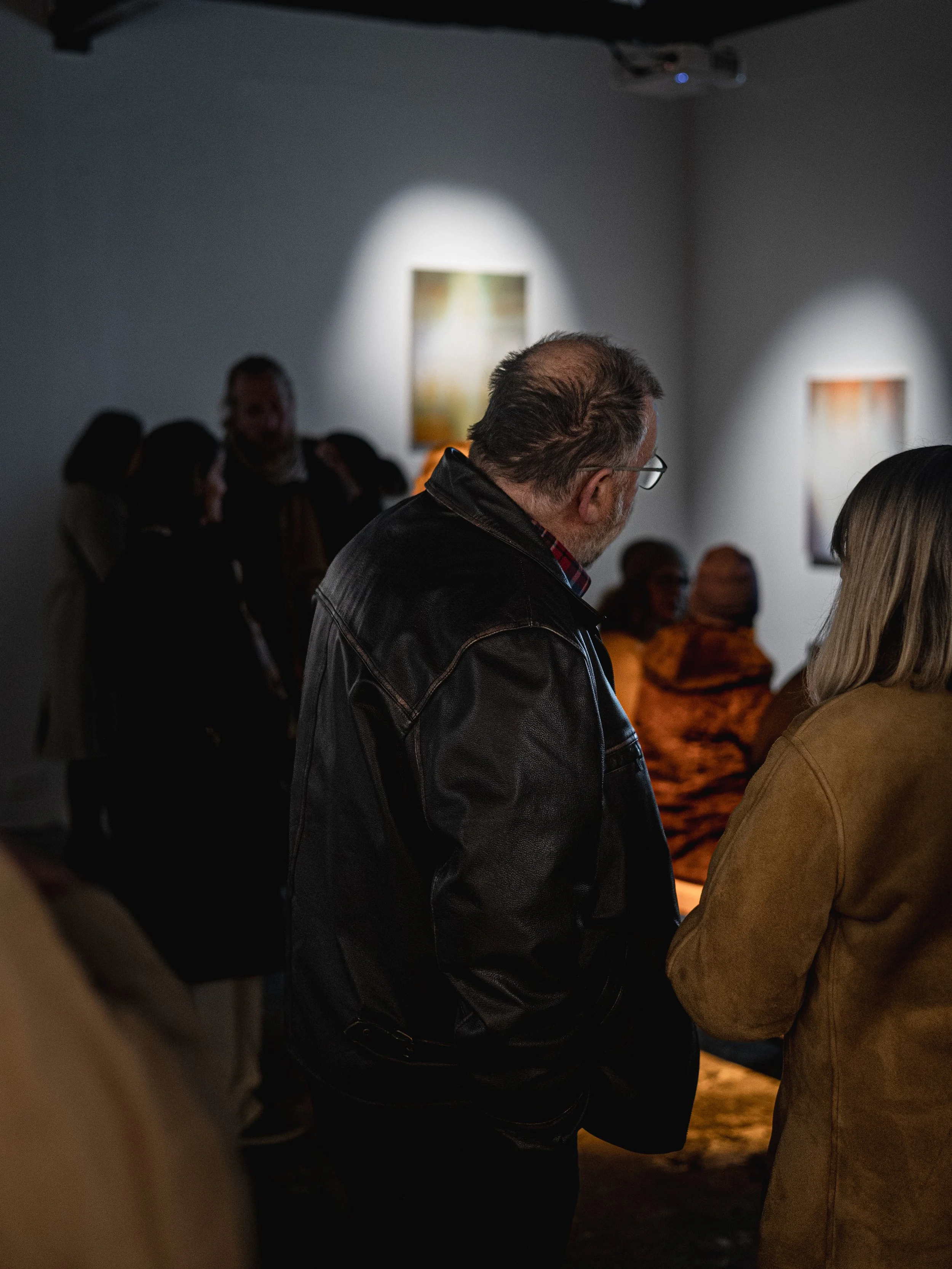 People viewing artwork in an art gallery or museum, with paintings illuminated on the wall.