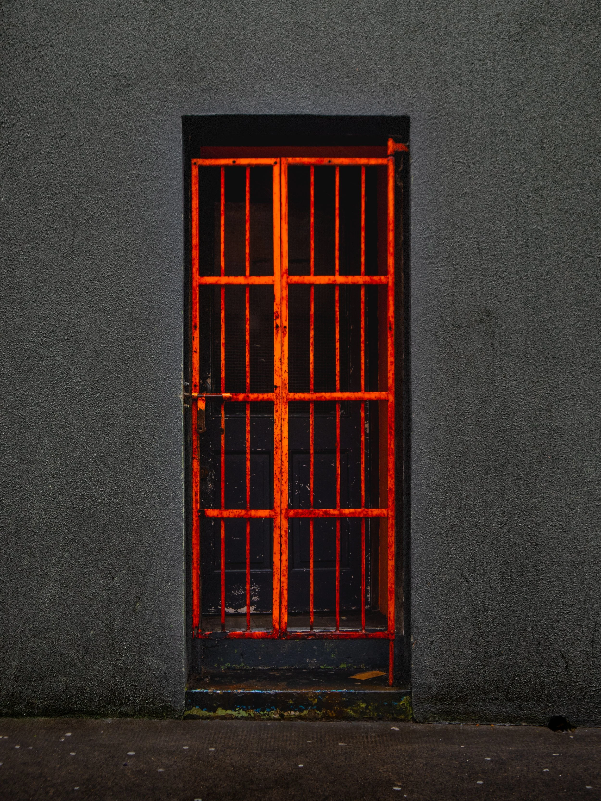 A metal door with red bars, set in a dark gray wall, illuminated by a red light.