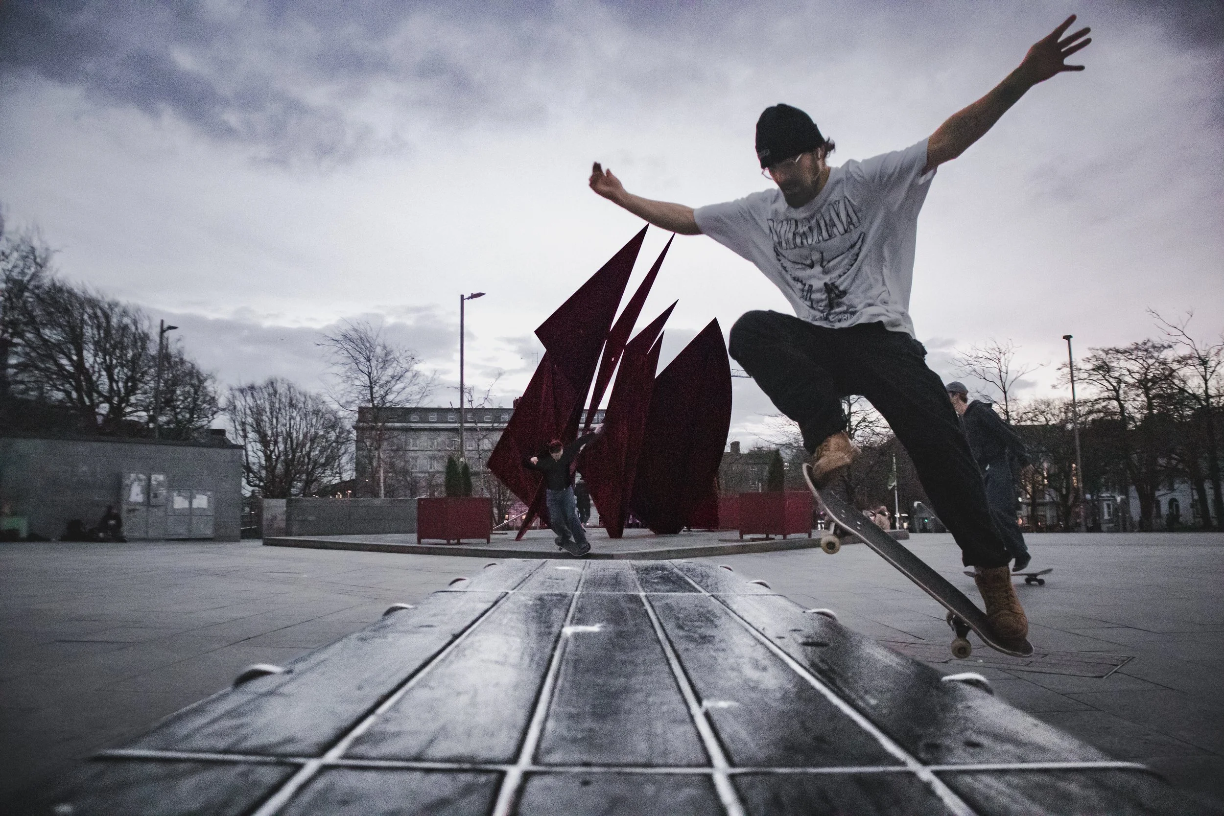 Skateboarder performing trick on a ledge with a modern outdoor sculpture in the background, overcast sky.