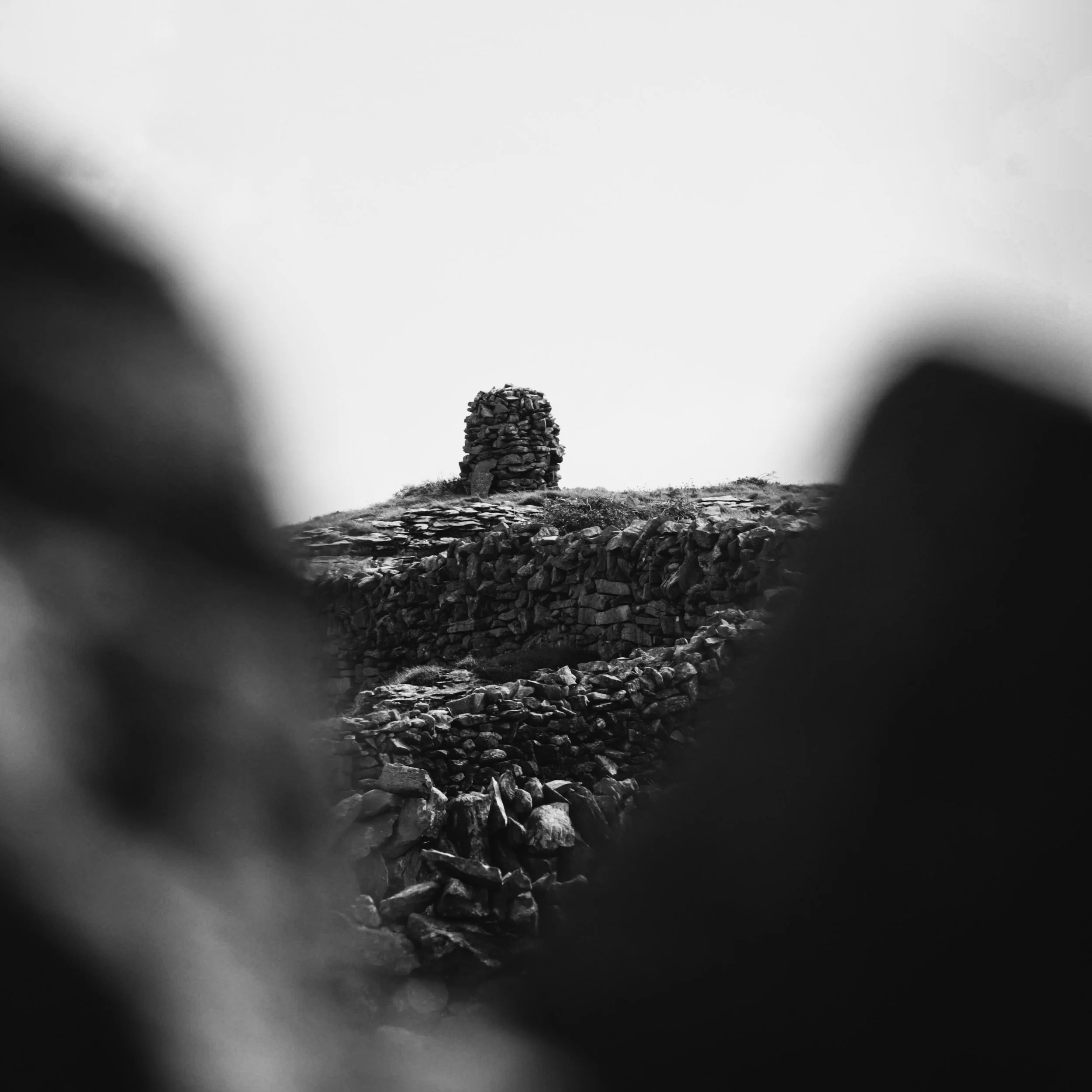 Black and white photo of a stone cairn on a rocky hilltop with blurred rocks in the foreground.