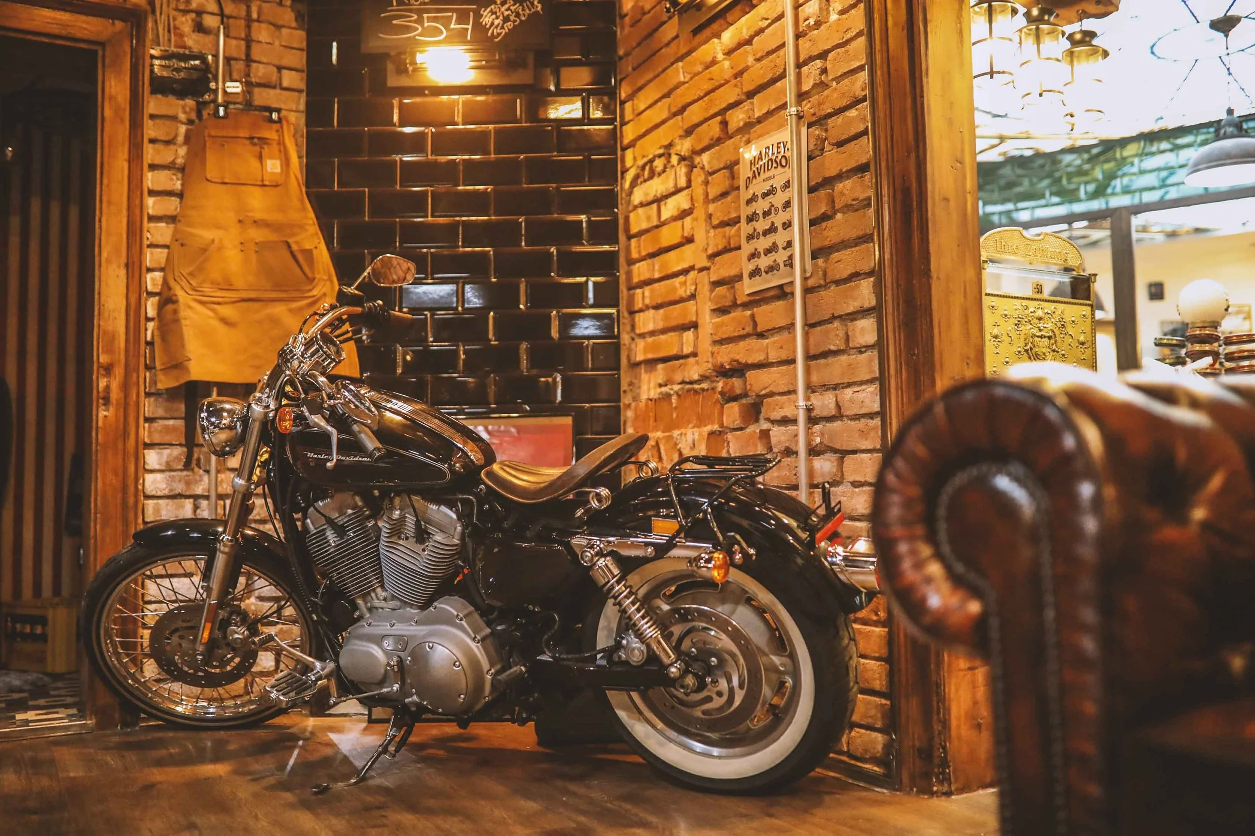 Ein schwarzes Harley-Davidson Motorrad ist auf einem Holzboden in einem rustikalen, gemütlichen Raum mit Ziegelsteinwänden abgestellt.