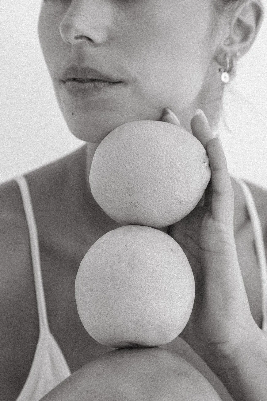 Black and white close-up image of a woman holding three round objects stacked vertically near her face, with only part of her face visible from the nose down.