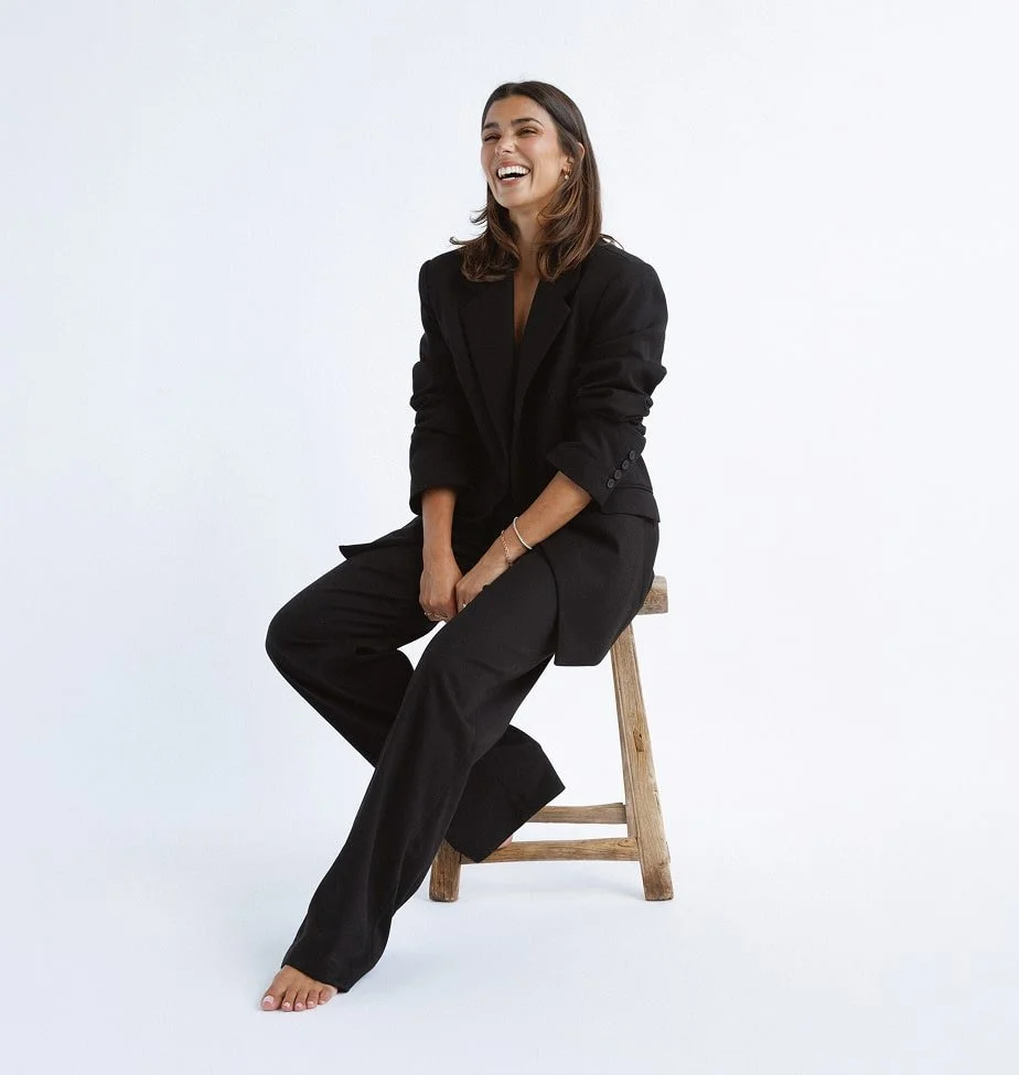 Bianca sitting on a stool, in a black suit smiling