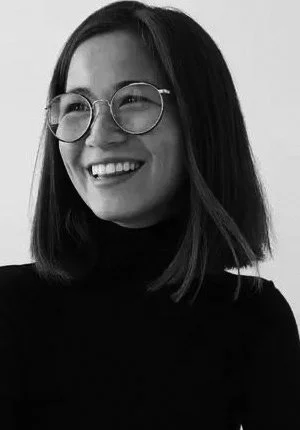 A smiling woman with shoulder-length dark hair, glasses, and a black turtleneck
