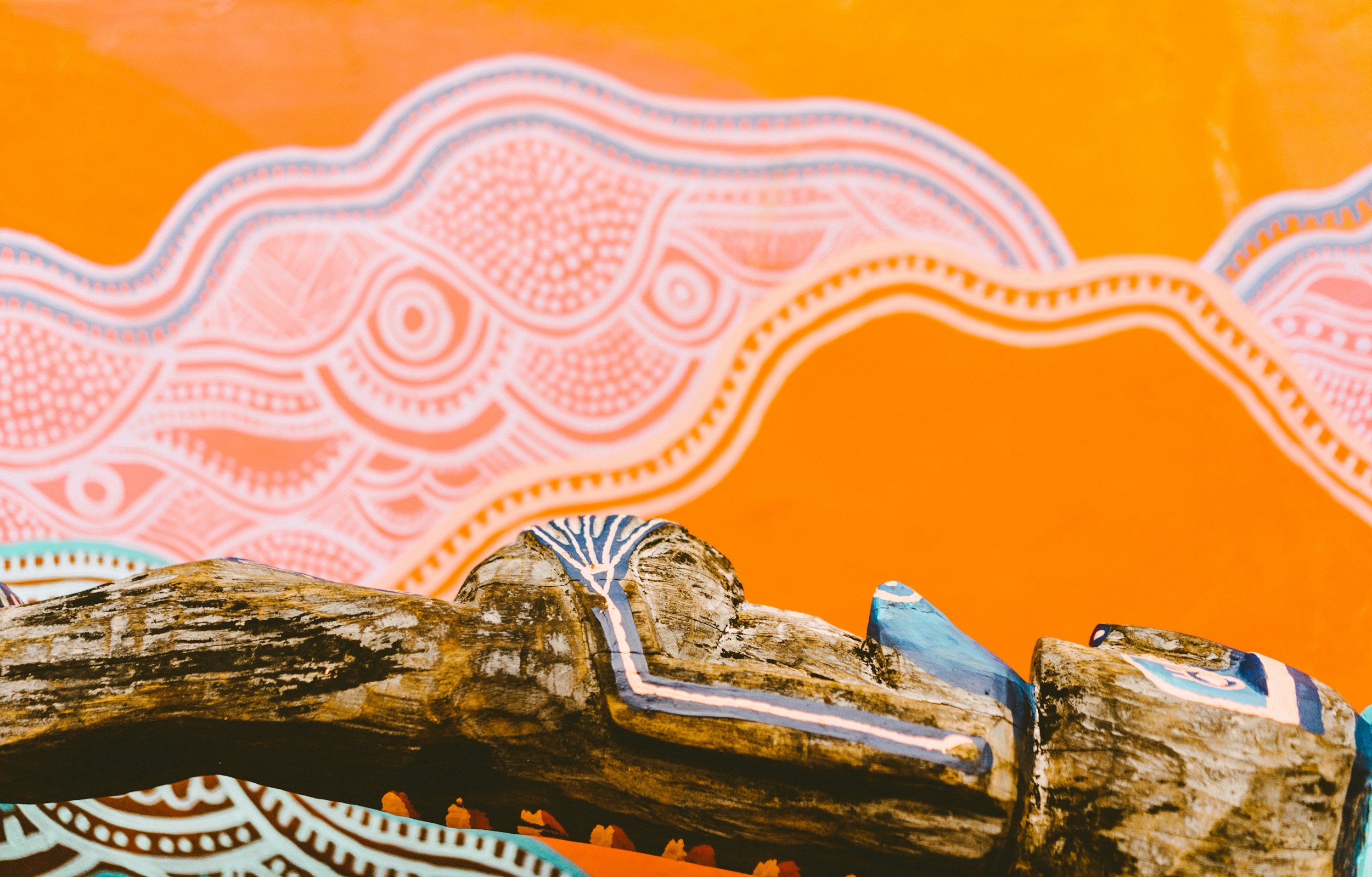 Painted driftwood on orange background with abstract white and dark blue patterns.