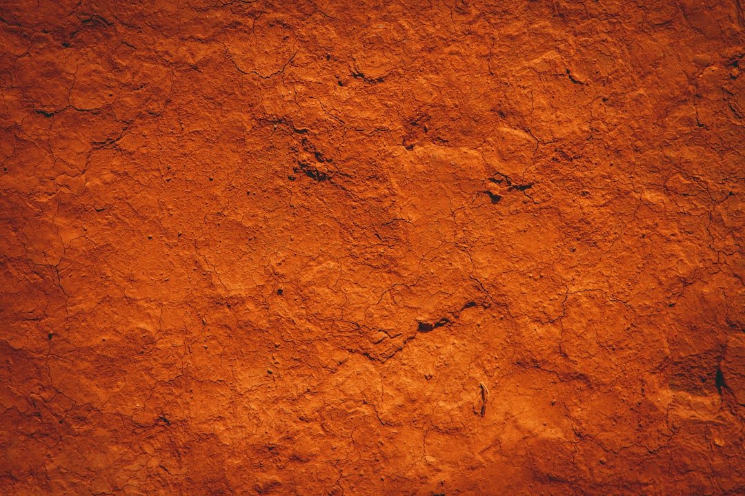 Close-up of cracked, orange-colored soil or clay surface.