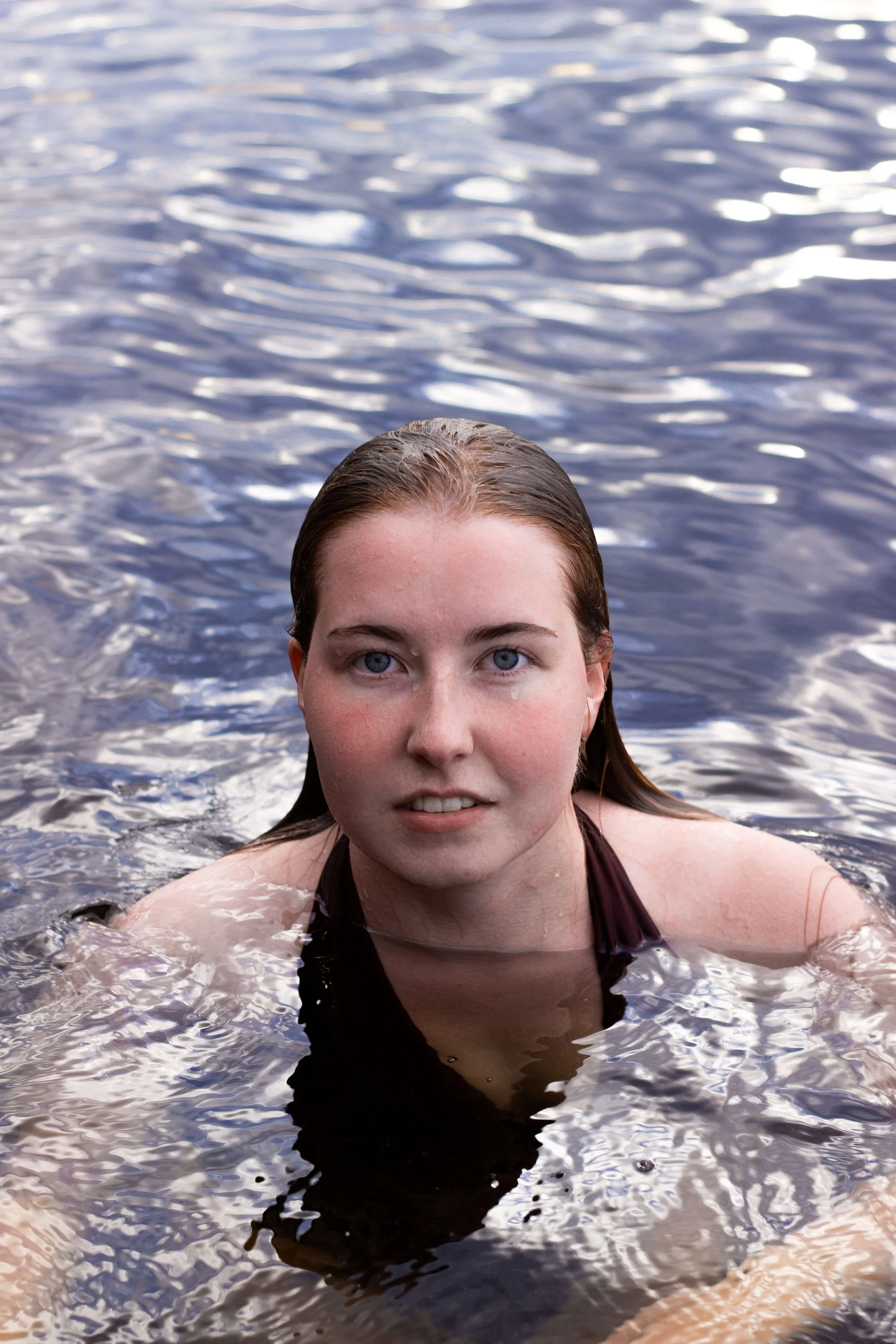A woman with wet hair swimming in a body of water, looking directly at the camera.