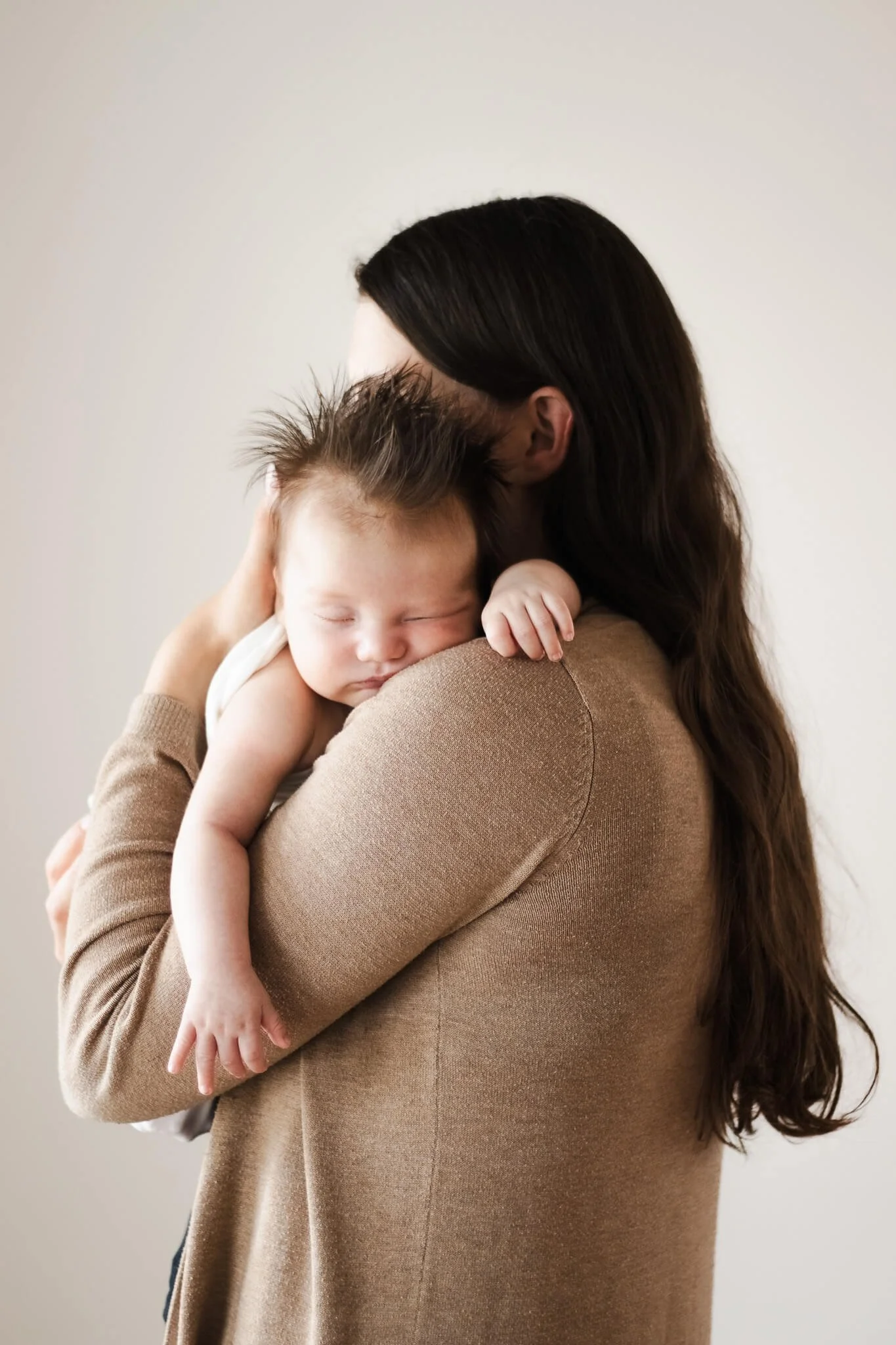 A woman with long dark hair holding a sleeping baby with spiky hair close to her chest