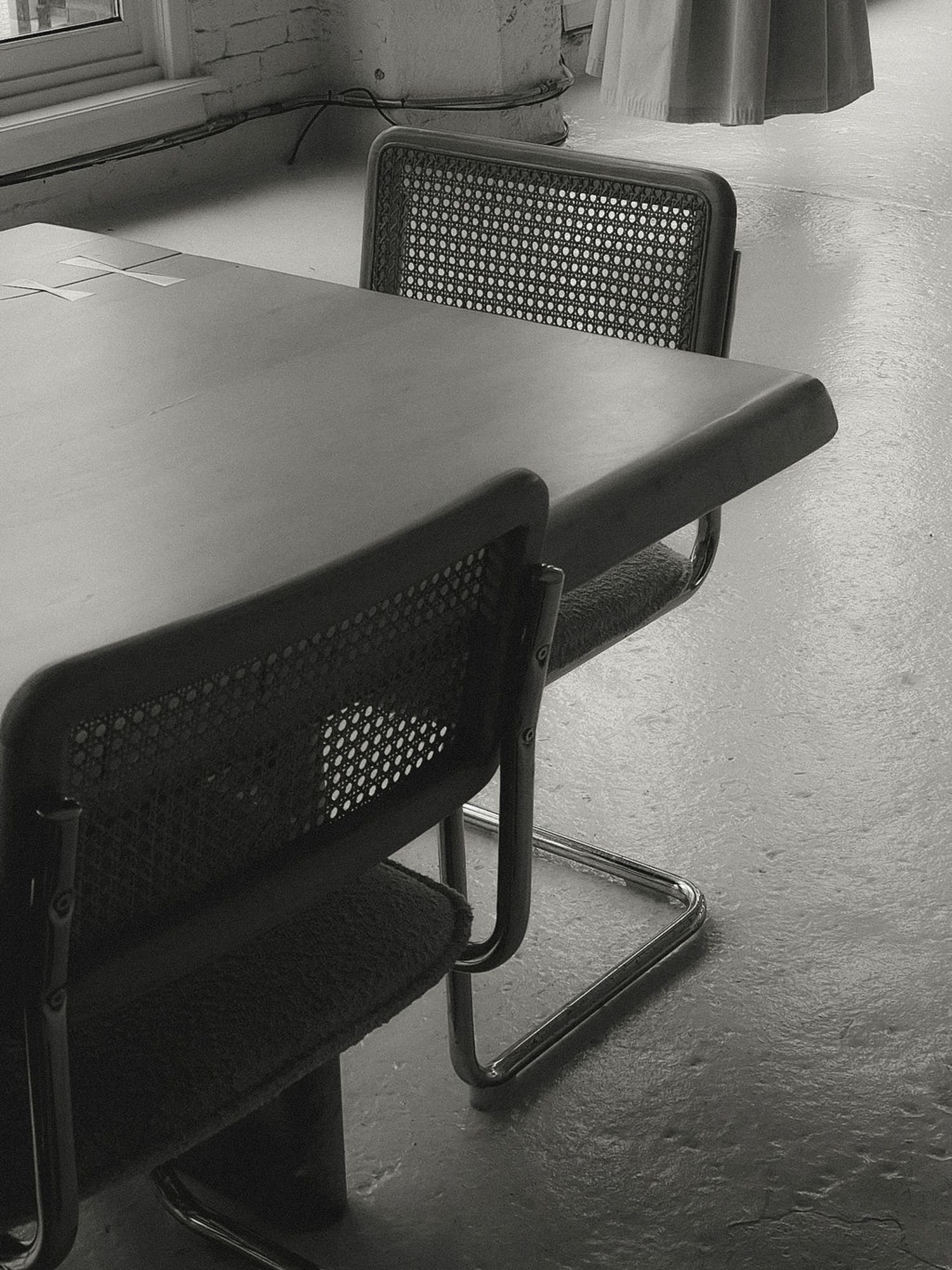 A black and gray office conference table with matching chairs in an industrial setting, with a brick wall, window, and curtains in the background.