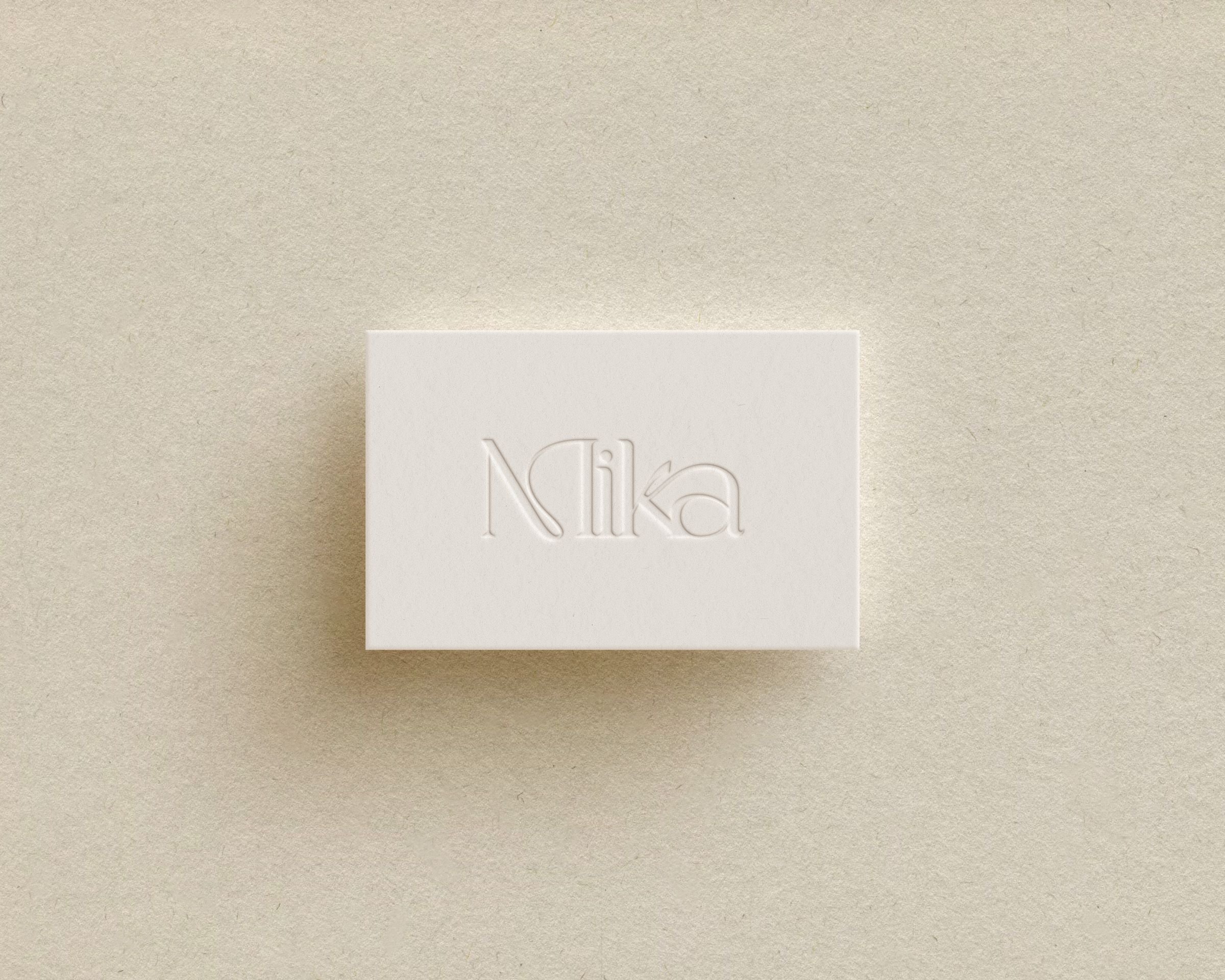 Brand mockup white embossed paper with the word 'Mika' on a beige textured background.