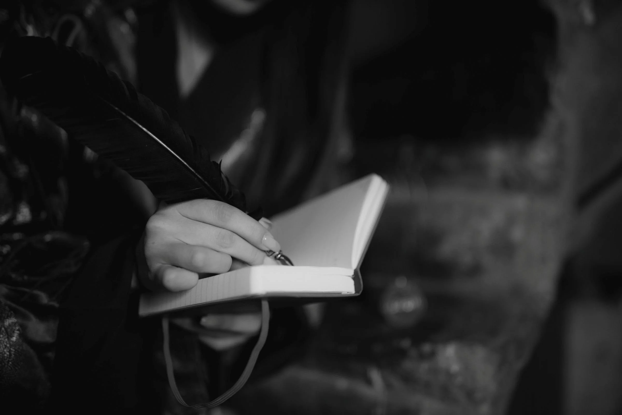 A person writing in a small notebook with a pen, in black and white.