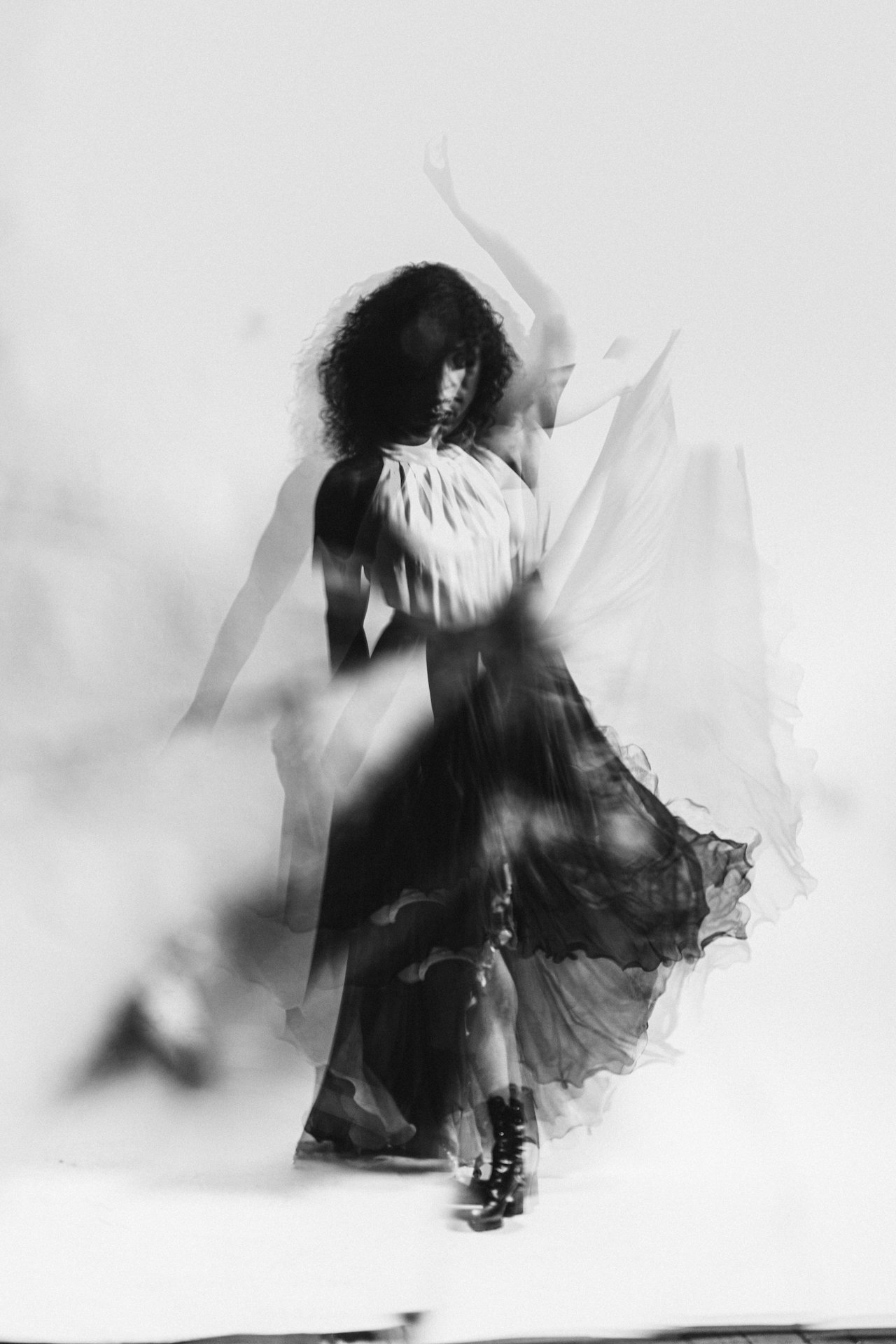 Black and white photo of a woman dancing in a flowing dress with a blurred motion effect.