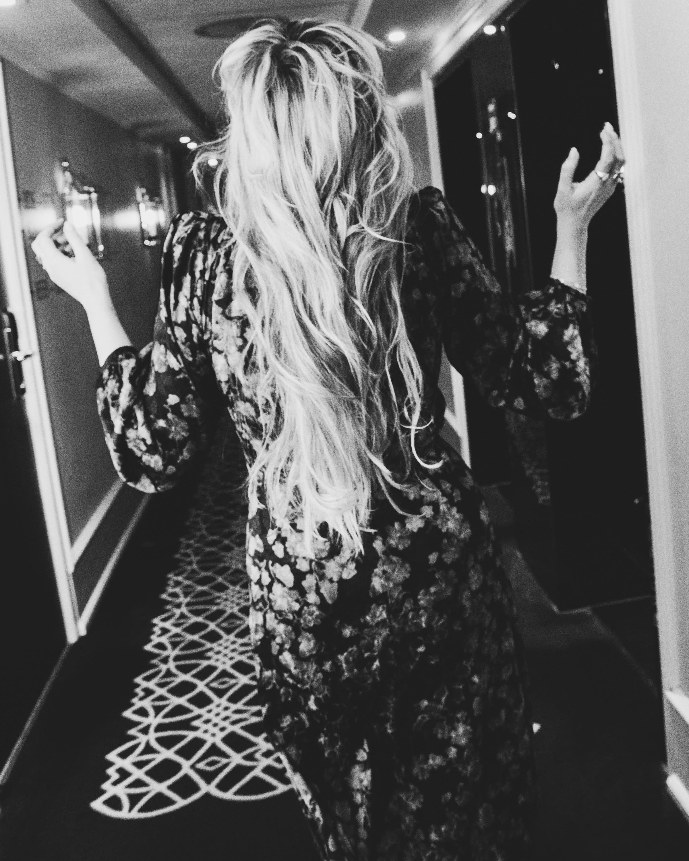 Nina Knag with long, wavy hair wearing a floral dress in a hotel hallway.